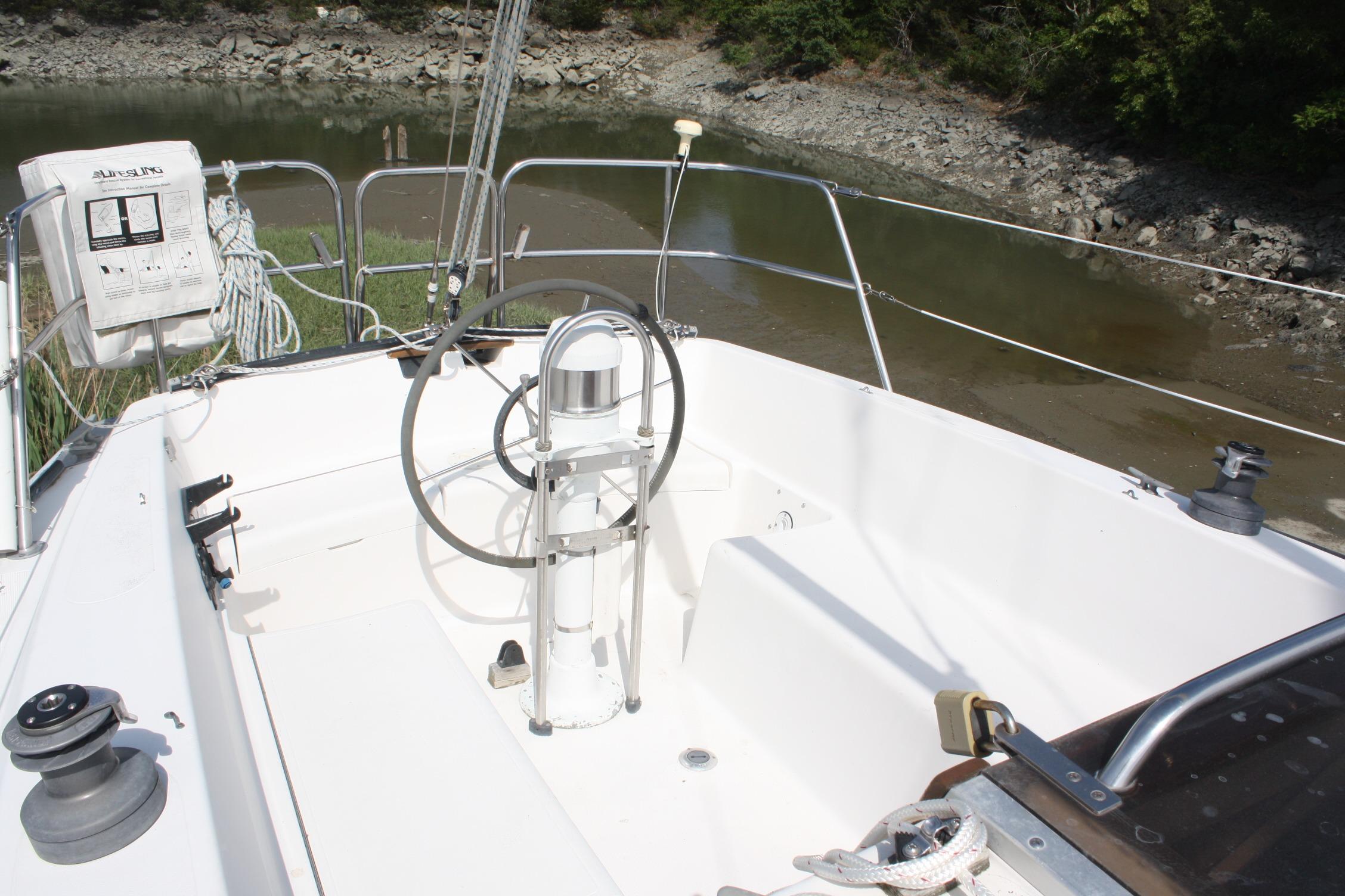 Cockpit of 1981 S2 9.2A sailboat with steering wheel and winches, docked by rocky shore.