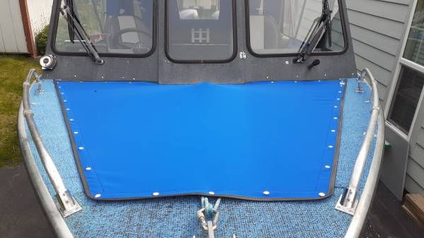 A boat with a blue cover and windows, docked at a pier.