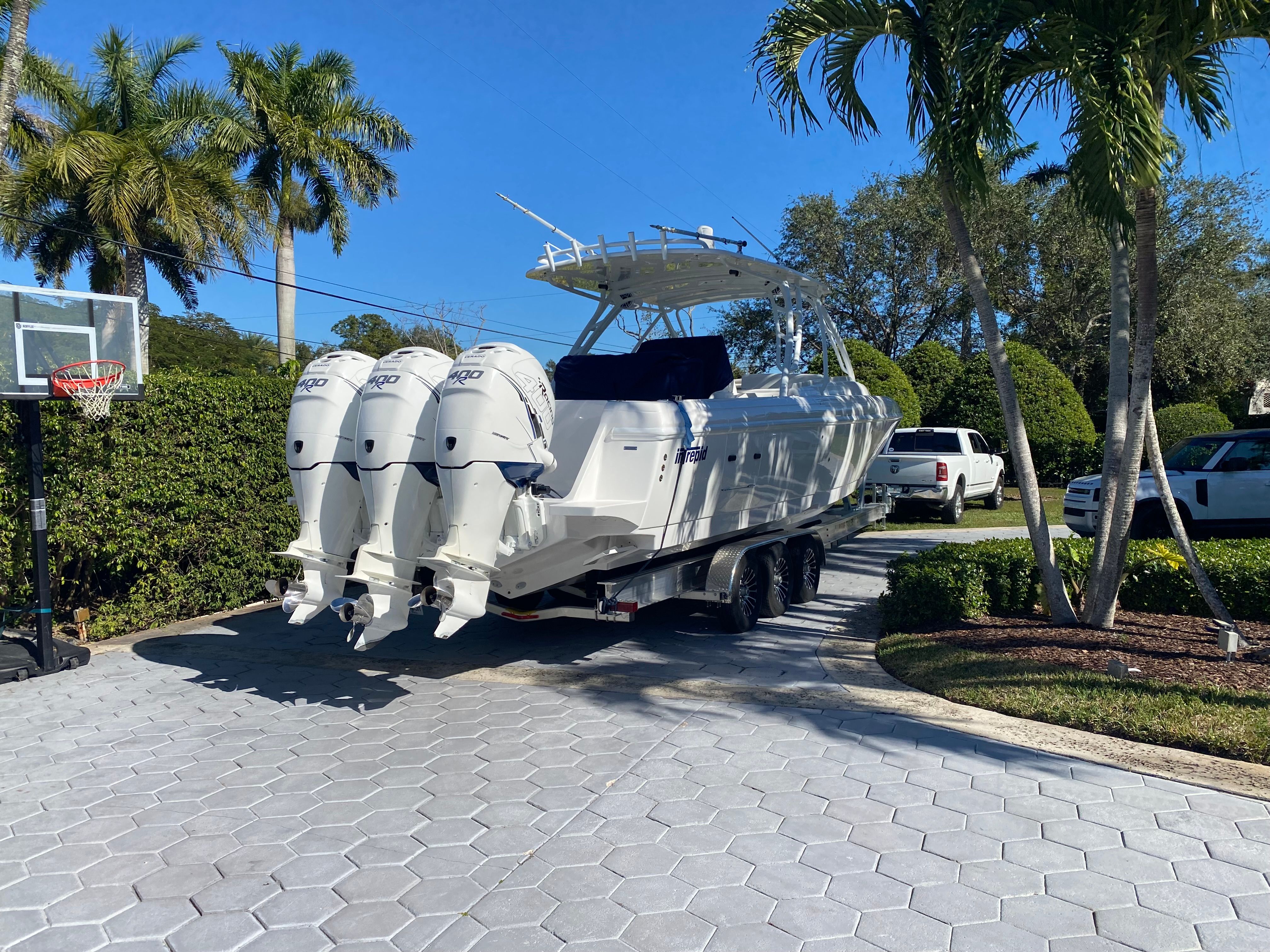 A 2011 Intrepid 37 boat on a trailer in a driveway, surrounded by palm trees.