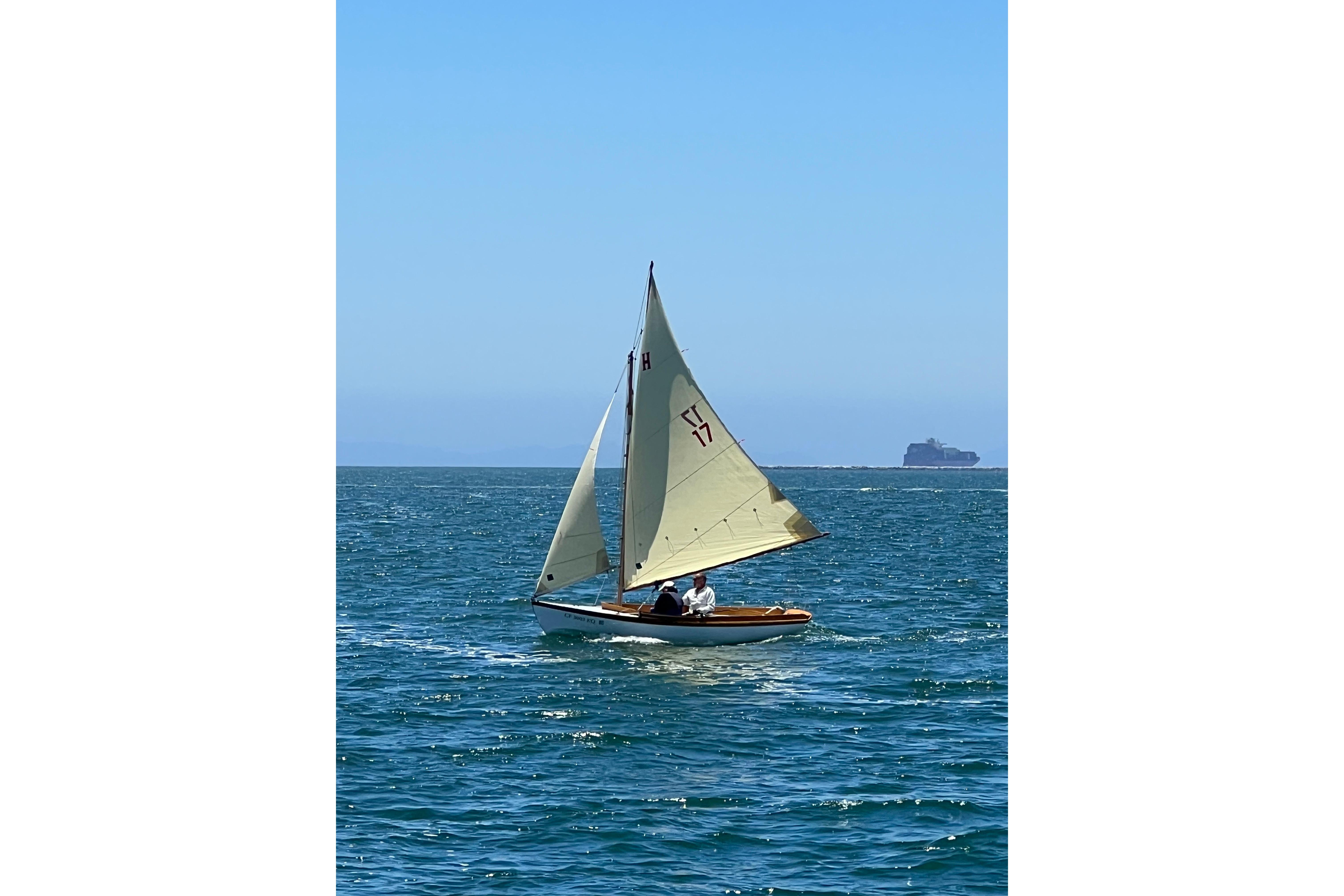 1920 Herreshoff 12.5 sailboat gliding on blue ocean under clear sky.