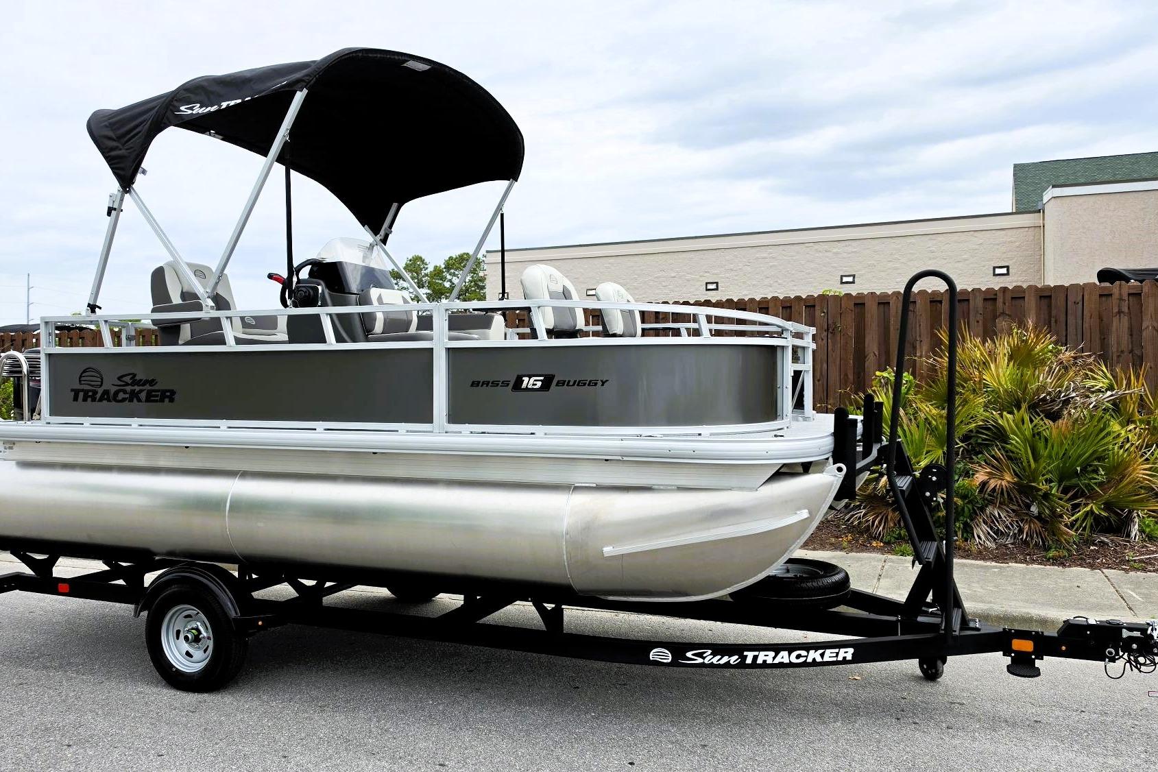 2026 Sun Tracker Bass Buggy 16 XL Select pontoon boat on trailer, parked outdoors.