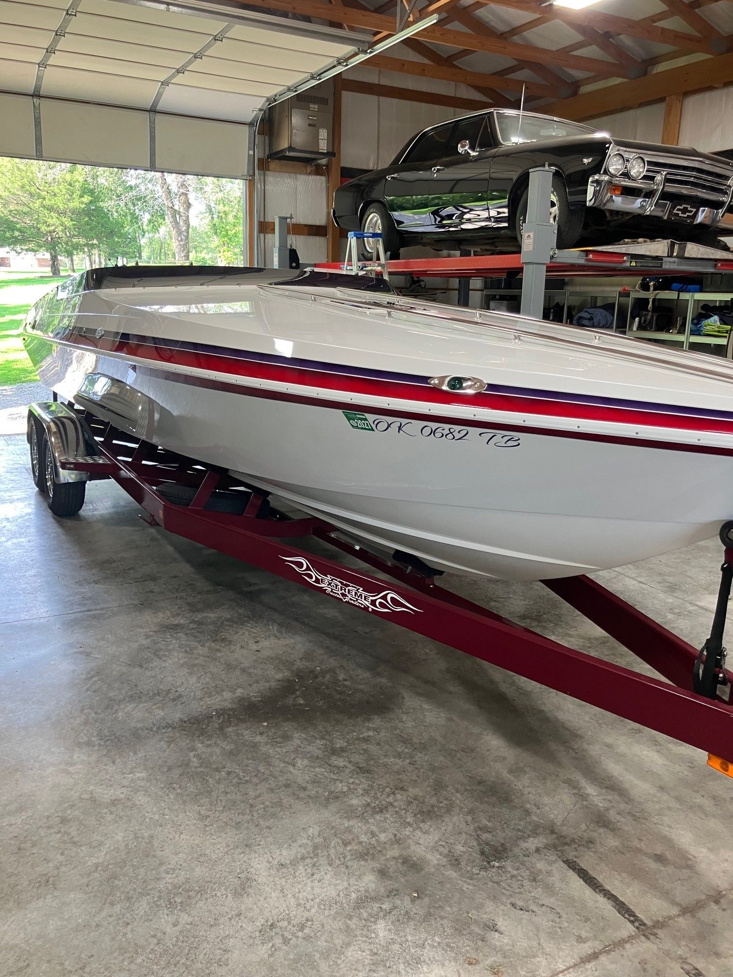 A white boat with red and blue stripes sits on a trailer in a garage.