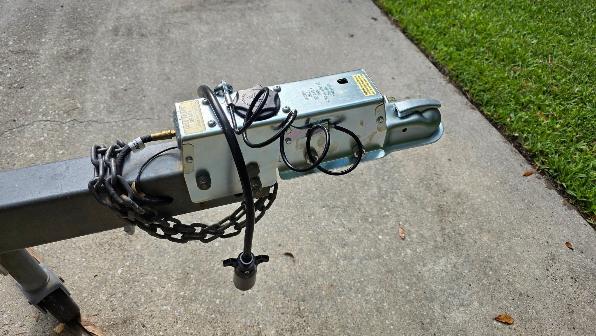 Close-up of a trailer hitch with chains and cables on a concrete surface.
