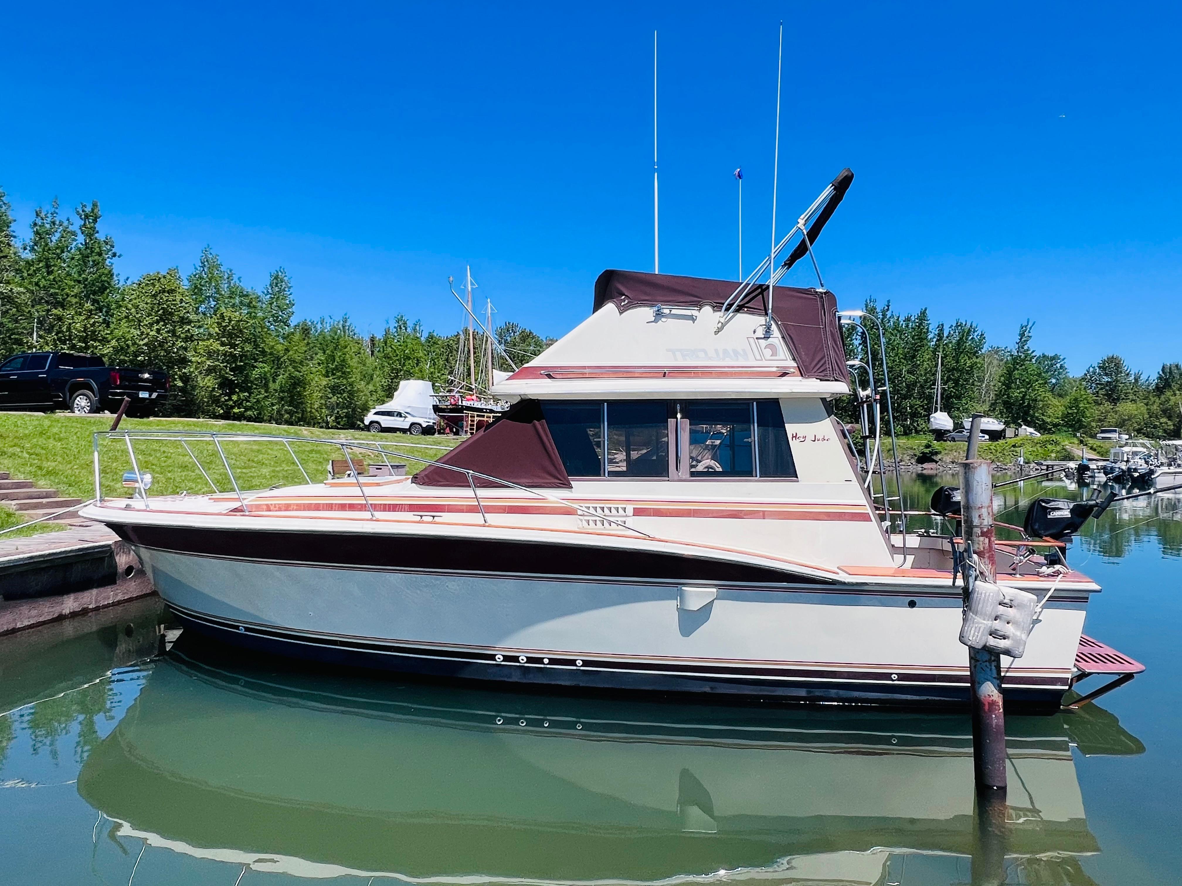 1982 Trojan F32 boat docked in a serene marina under a clear blue sky.