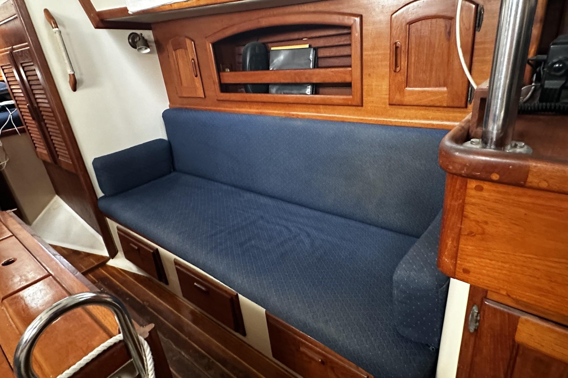 Interior of a 1990 Pacific Seacraft 34 sailboat with blue cushioned seating and wooden cabinetry.