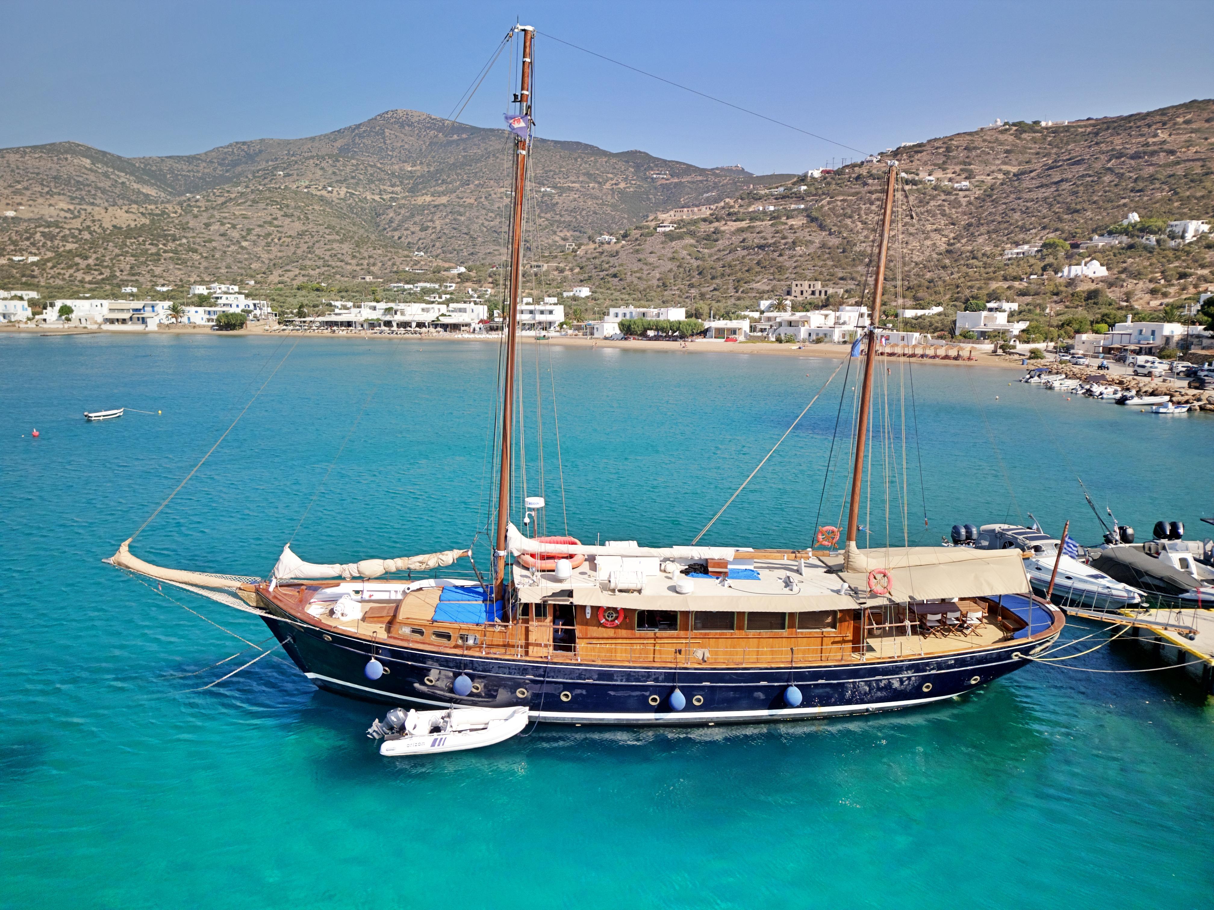 Vintage 1969 Psarros Shipyard yacht docked in clear turquoise waters, surrounded by scenic hills.