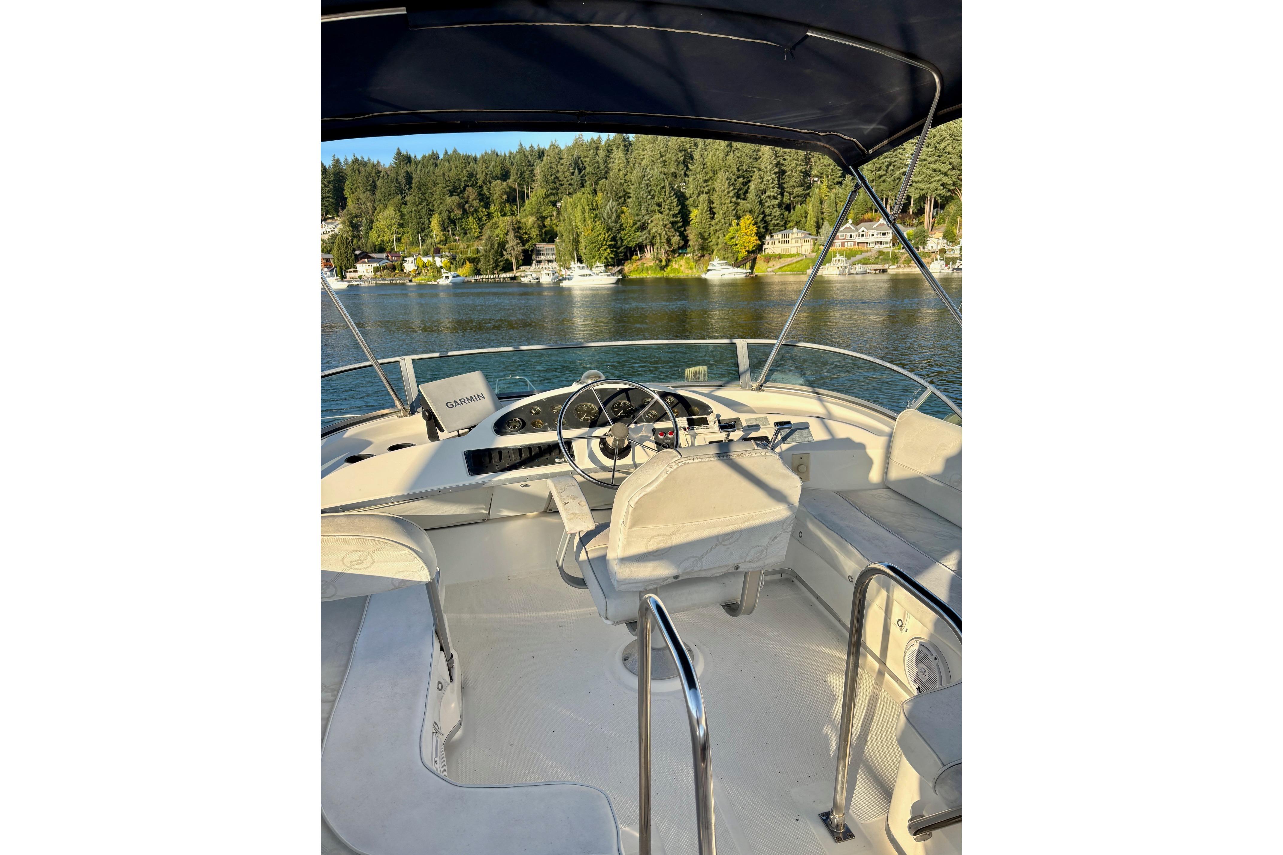1998 Bayliner 3388 Command Bridge Motoryacht interior with steering wheel, overlooking scenic waterway.