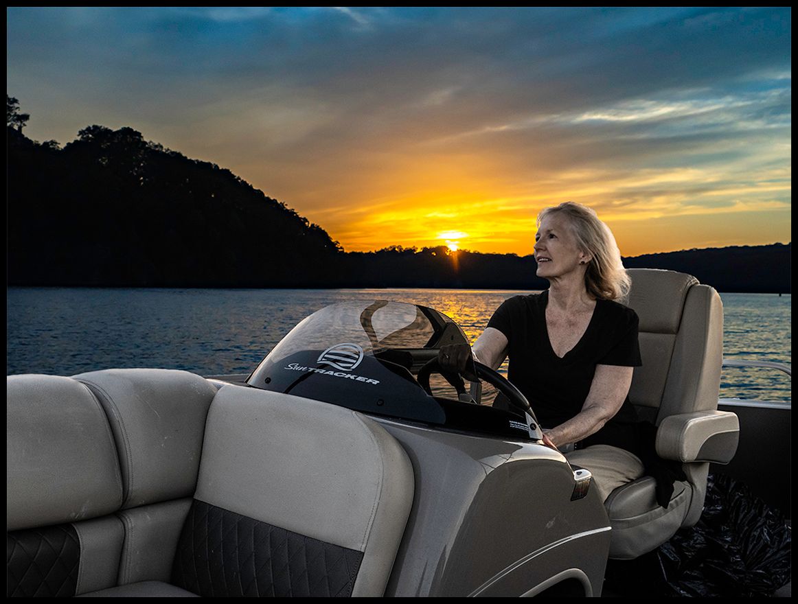 A woman sits on a boat at sunset on a calm lake.