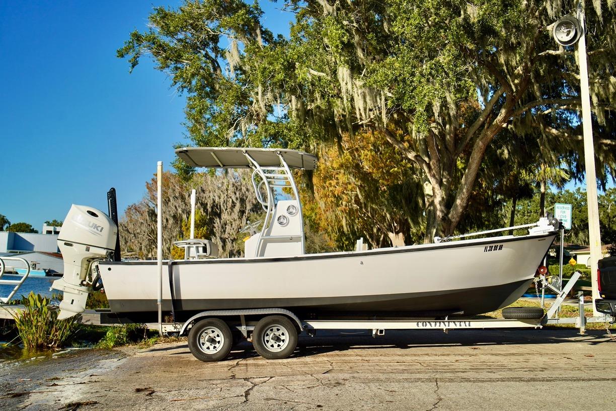 1970 Aquasport 222 Flatback boat on trailer, parked near water, surrounded by trees.