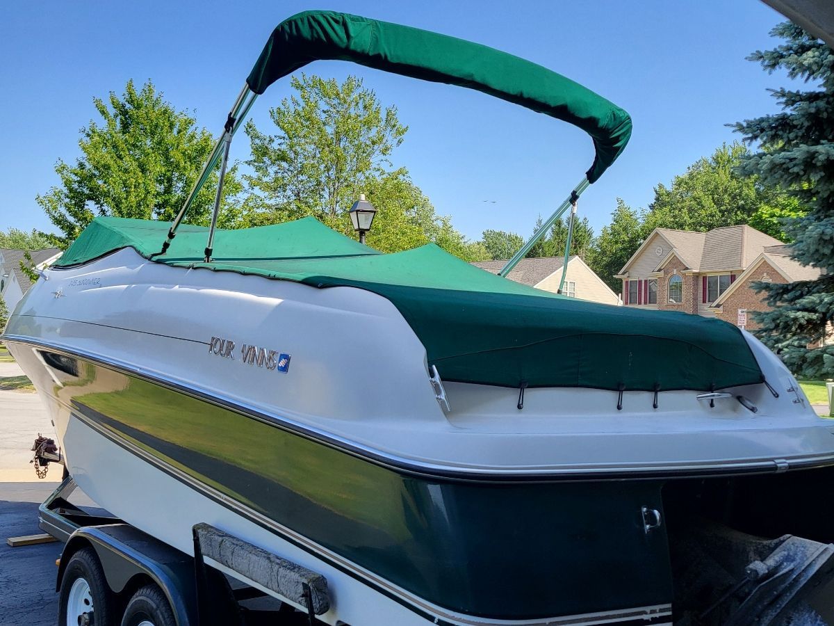 A 1996 Four Winns 245 Sundowner with a green cover, on a trailer in a residential area.