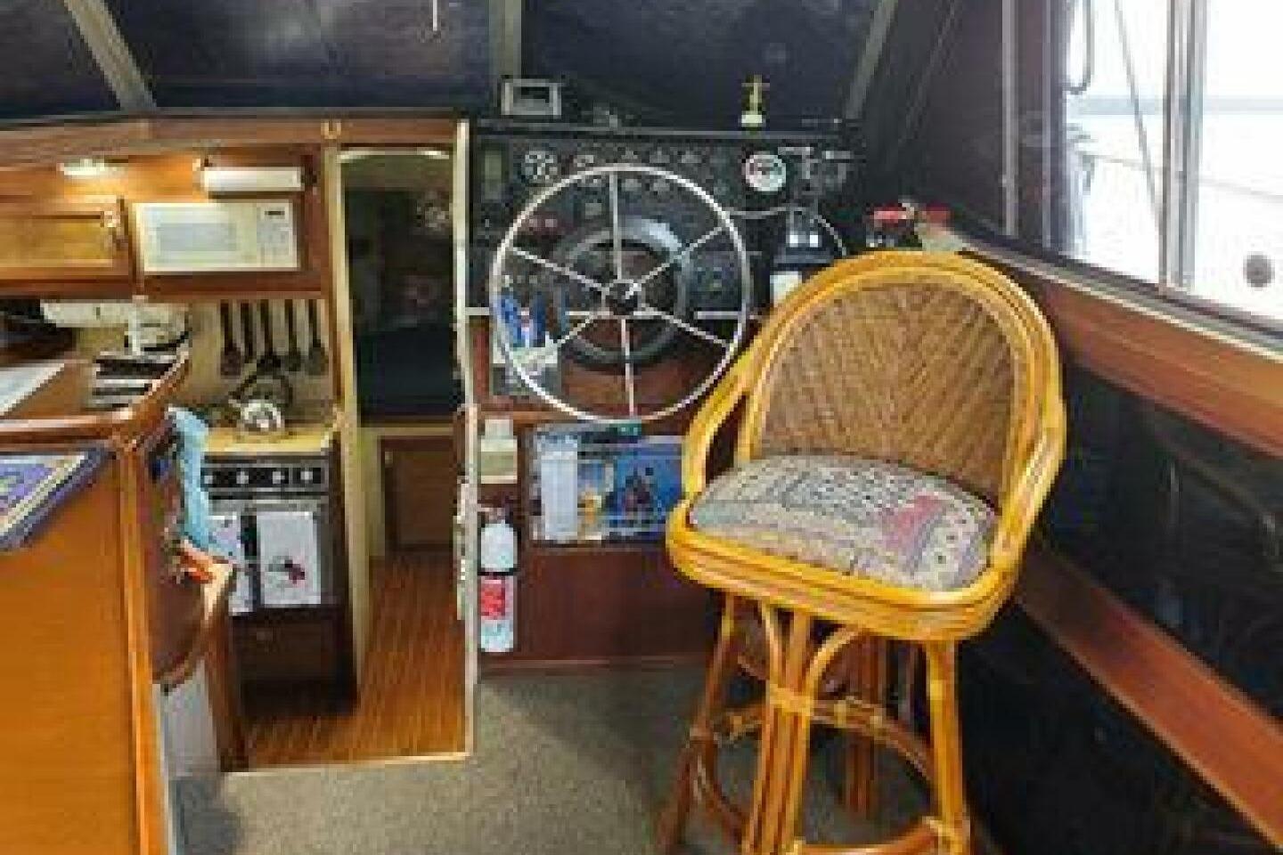 Interior of 1986 Bayliner 3270 Motoryacht with helm, wicker chair, and kitchen area.