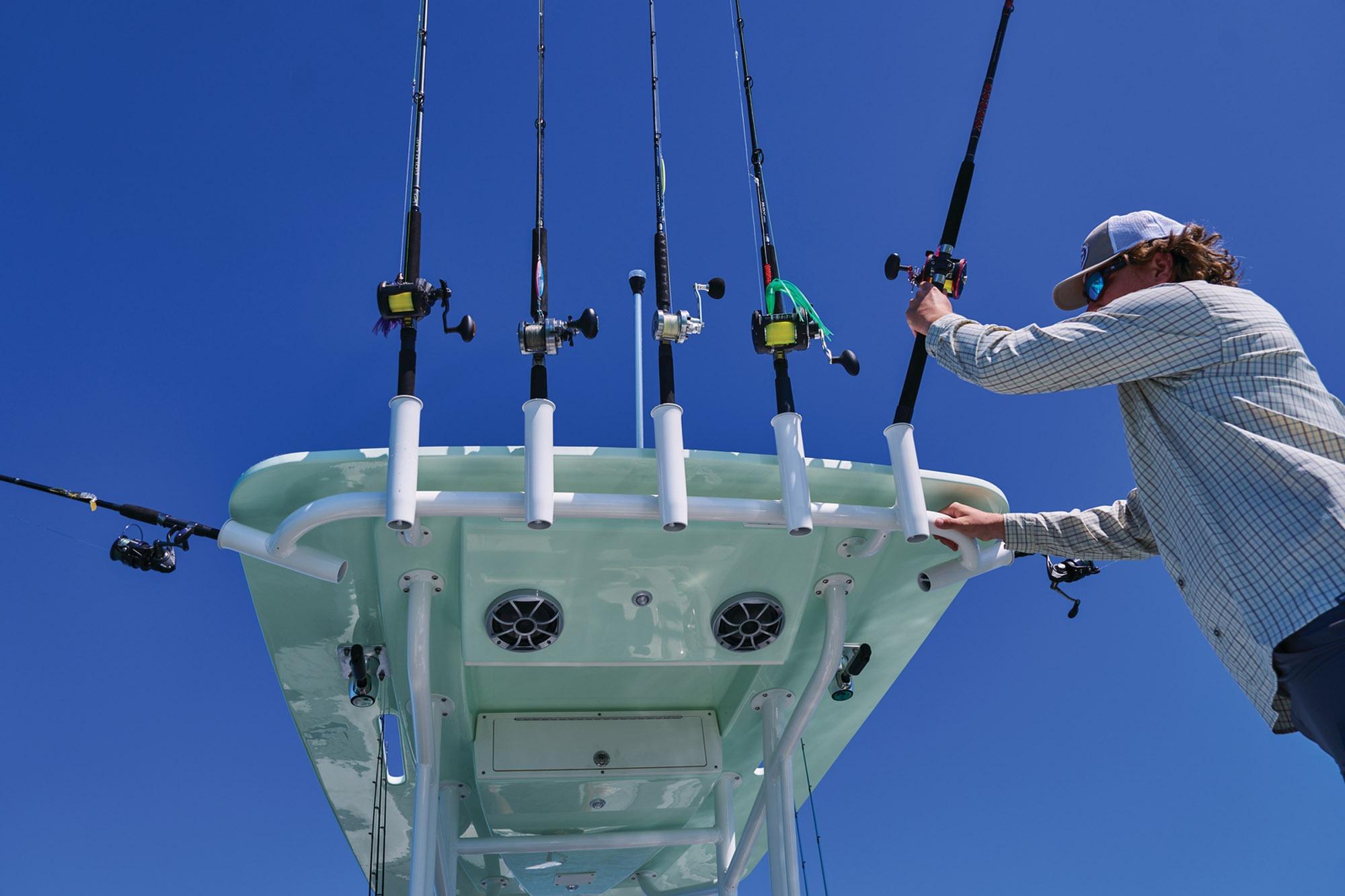 Man organizing fishing rods on Mako 24 APEX boat, 2026 model, under clear blue sky.