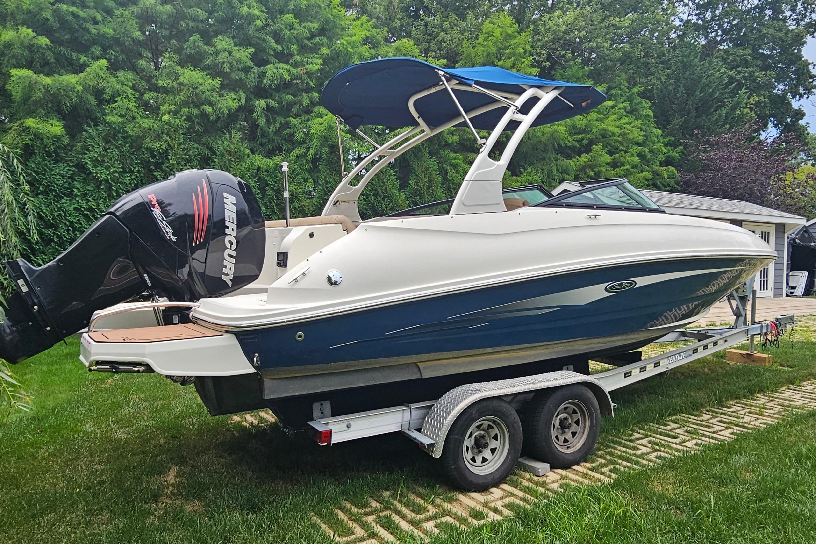 2017 Sea Ray SDX 240 Outboard boat on trailer, surrounded by lush greenery.
