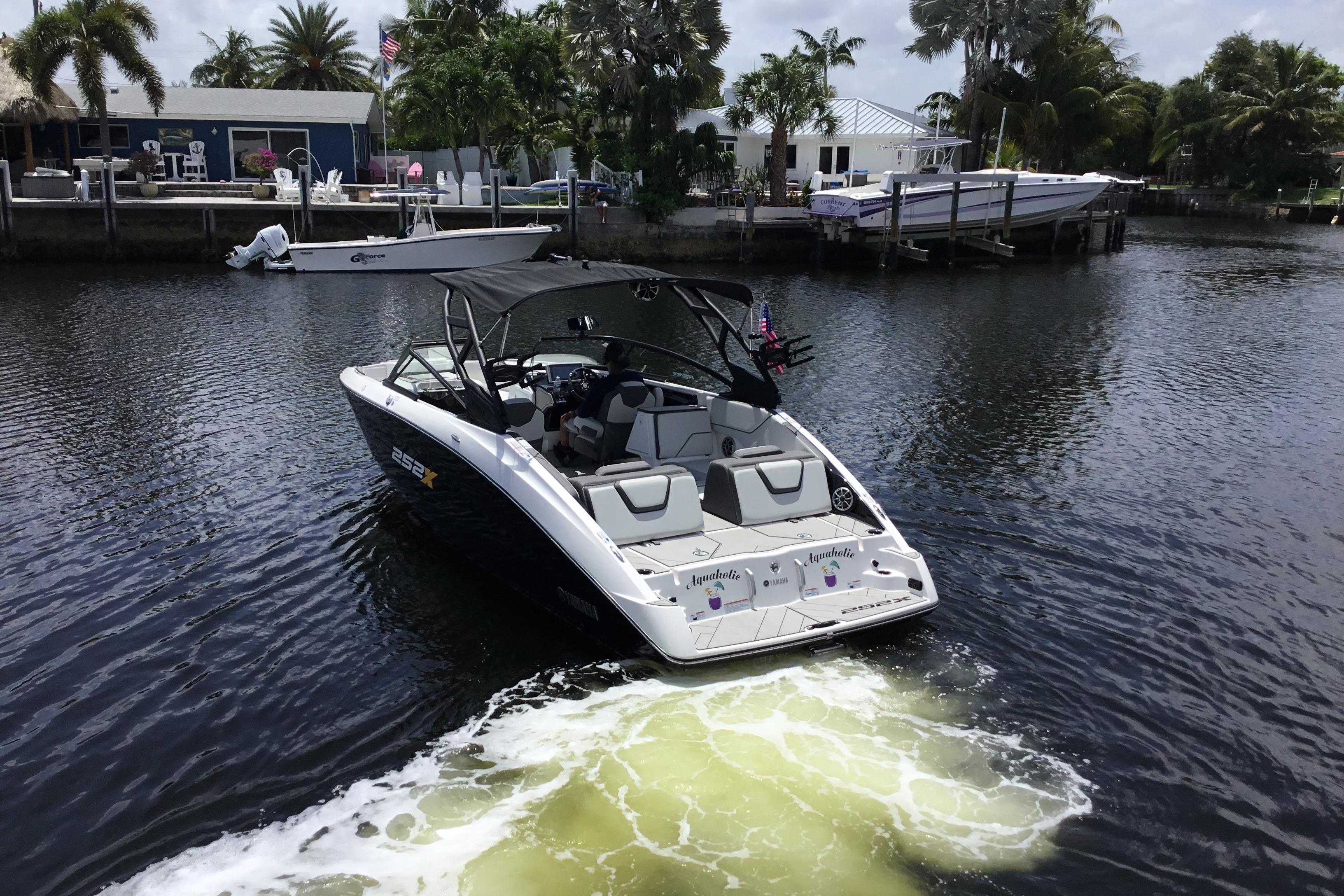 2023 Yamaha Boats 252XE cruising on a scenic waterway near a dockside home.