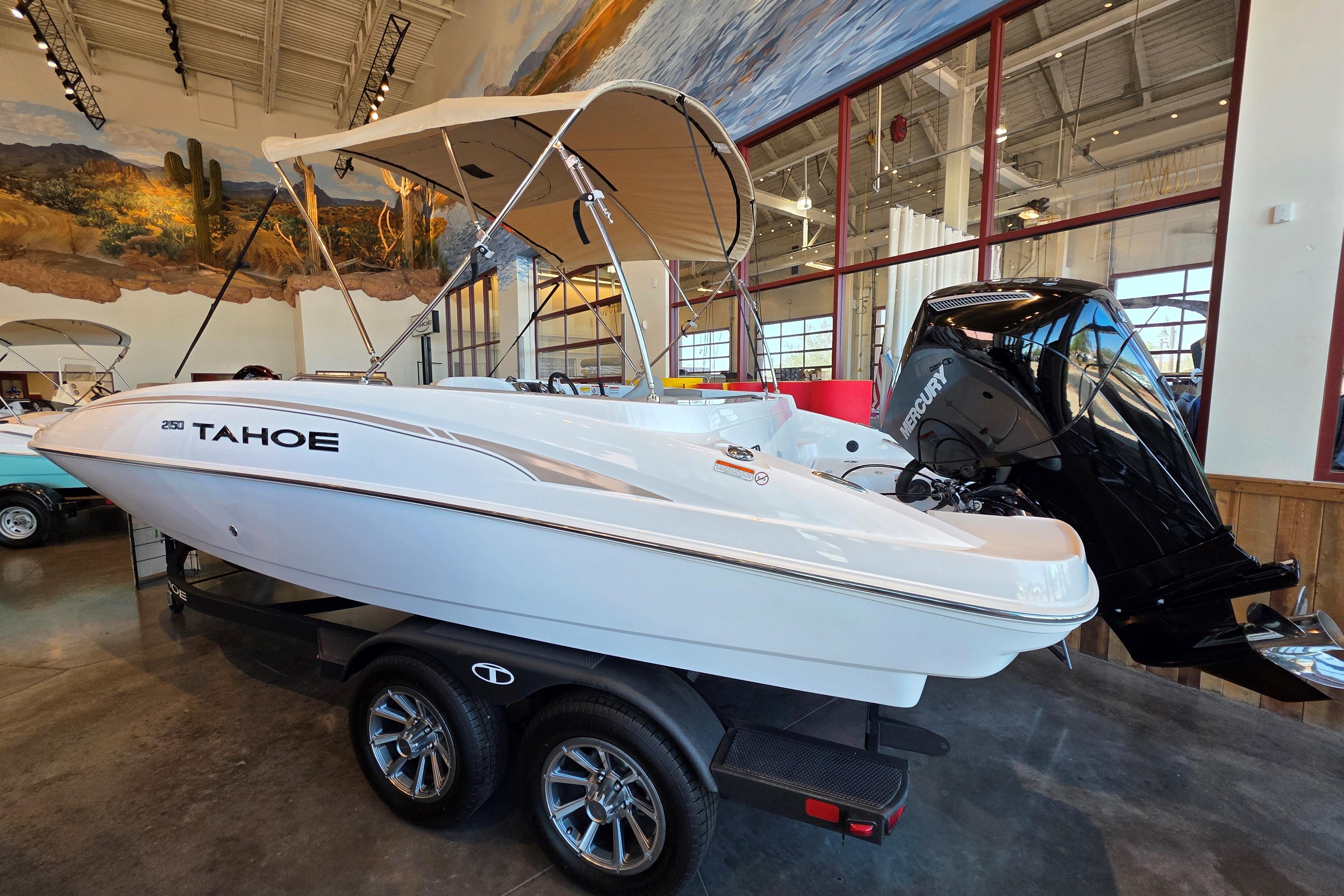 2026 Tahoe 2150 boat with canopy and Mercury engine on display indoors.