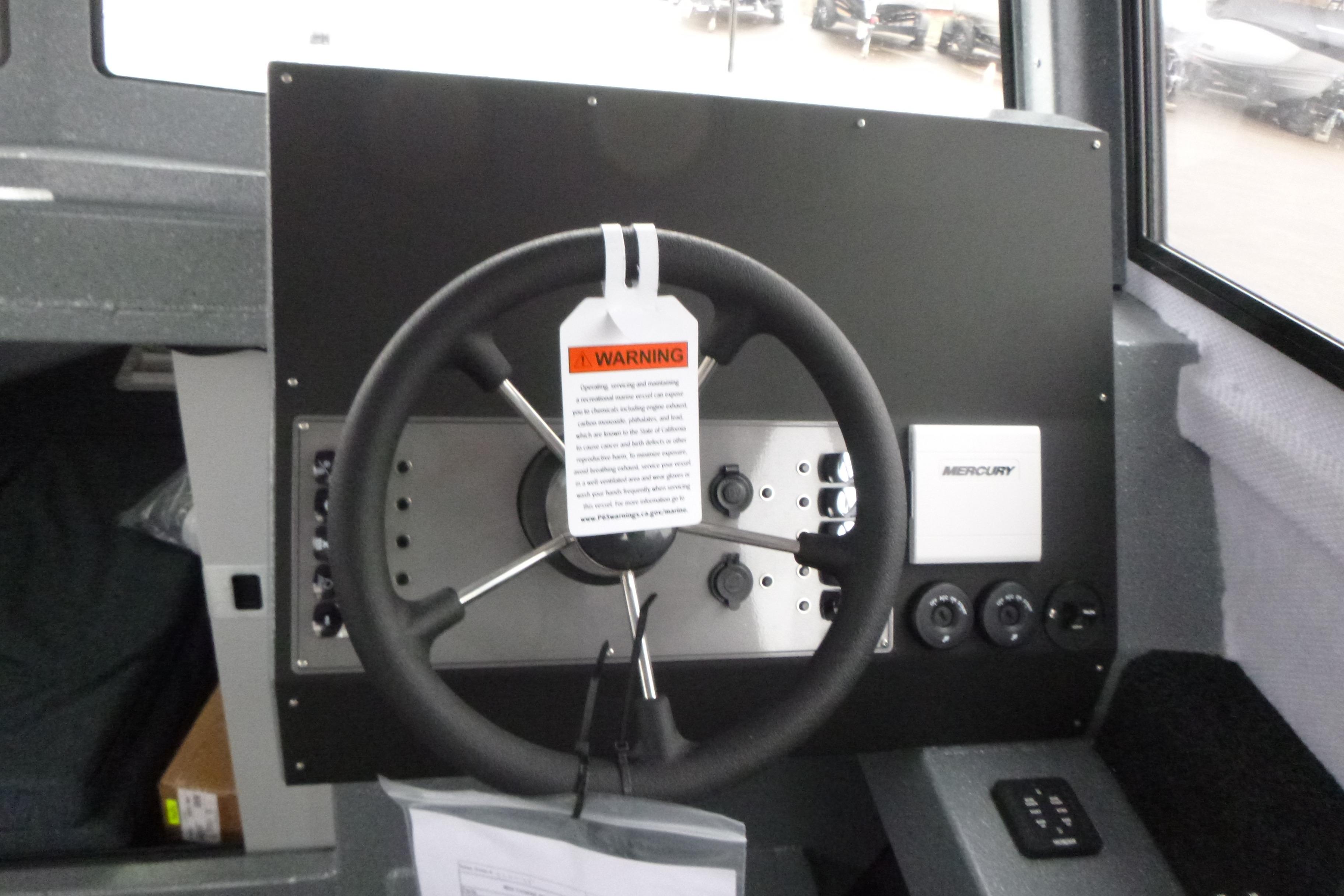 Steering wheel of 2026 KingFisher 25 XAC boat with Mercury controls and warning tag.