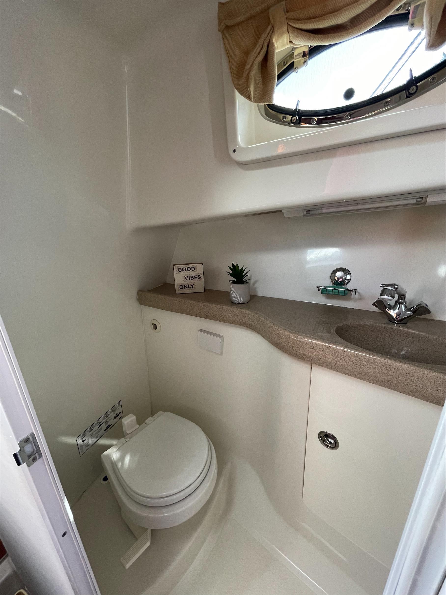 Interior of a boat cabin with a toilet, sink, and window.