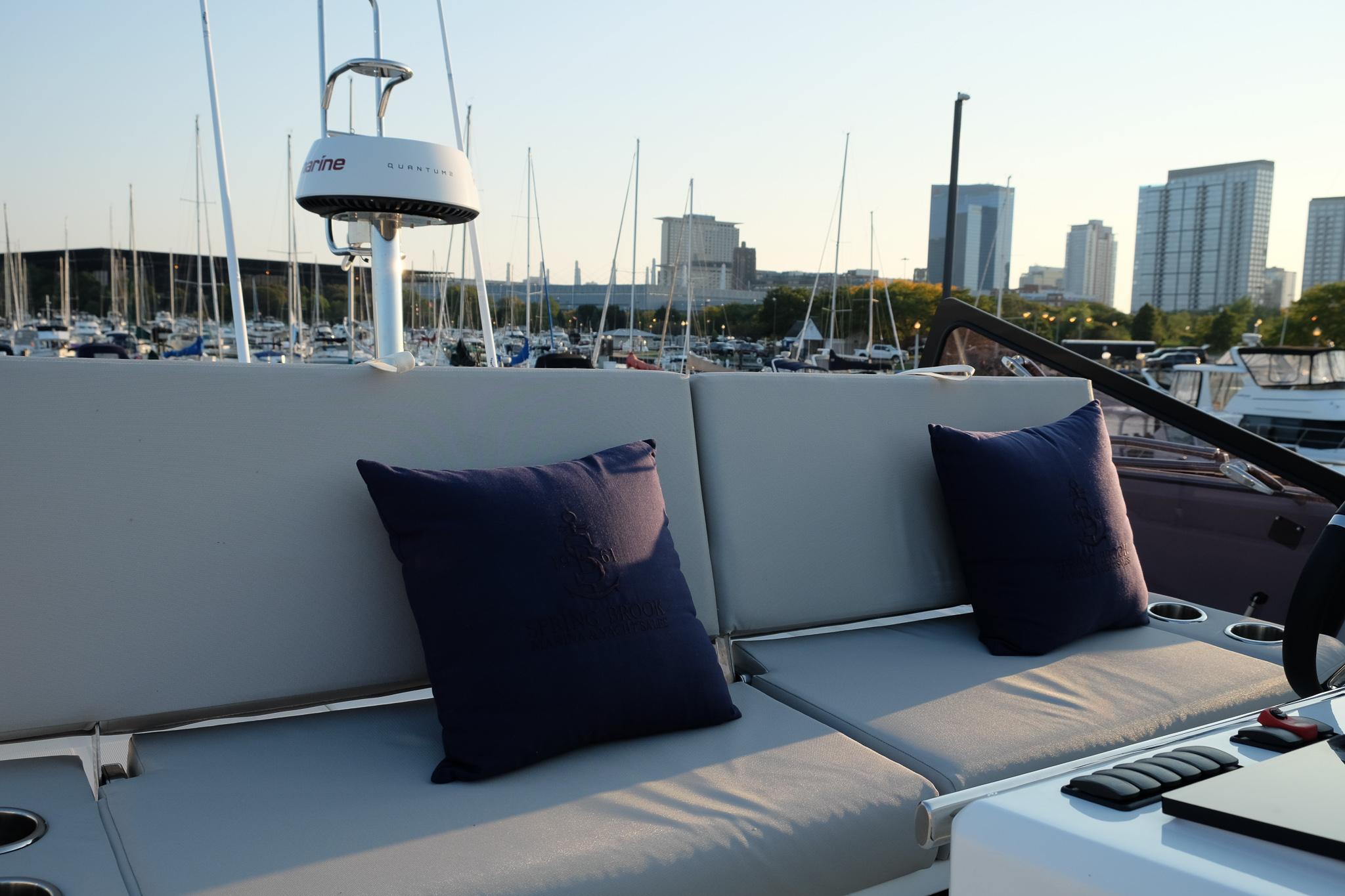 Prestige 590 Sport Fly 2021 yacht with cushions, marina view, and city skyline in background.