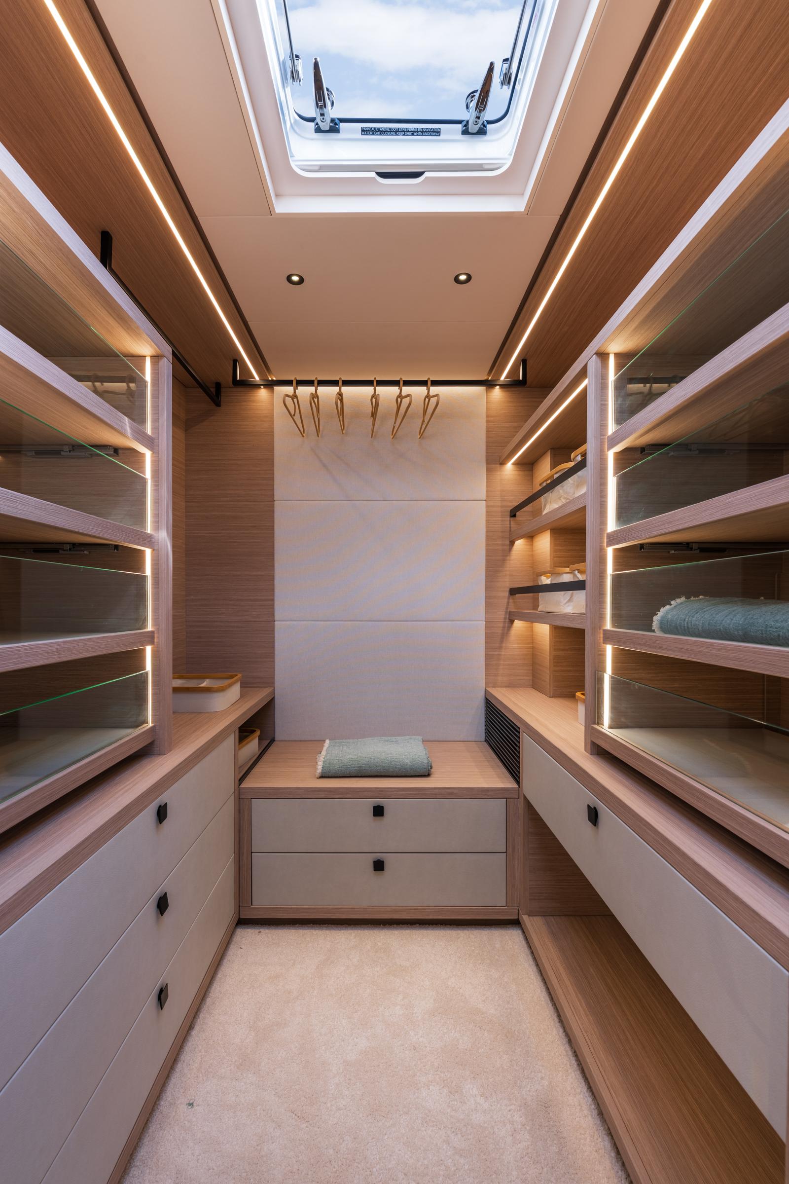 Luxurious walk-in closet on 2025 Lagoon Eighty 2 yacht with skylight and modern shelving.