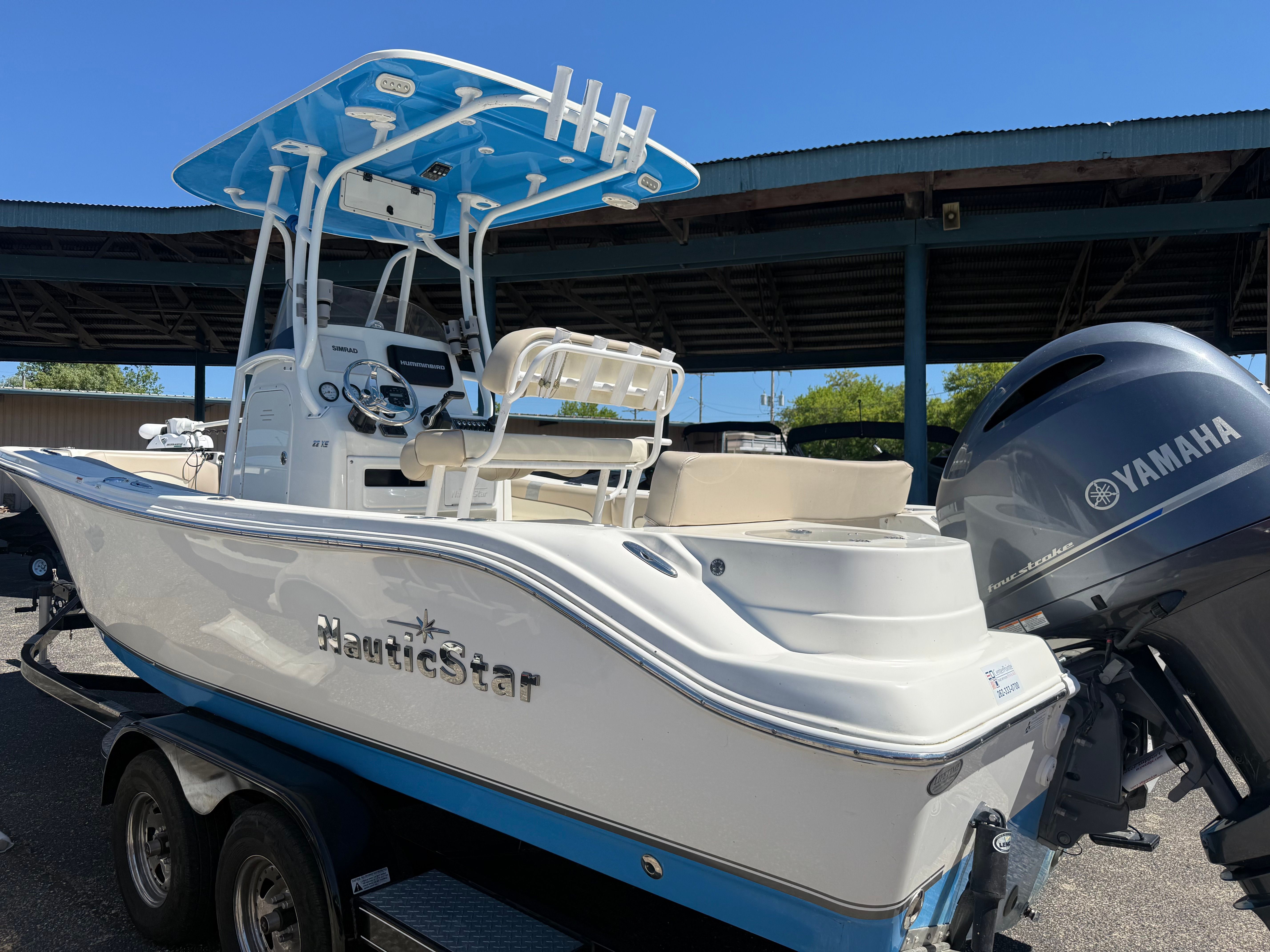 A white boat with blue accents is on a trailer under a covered area.