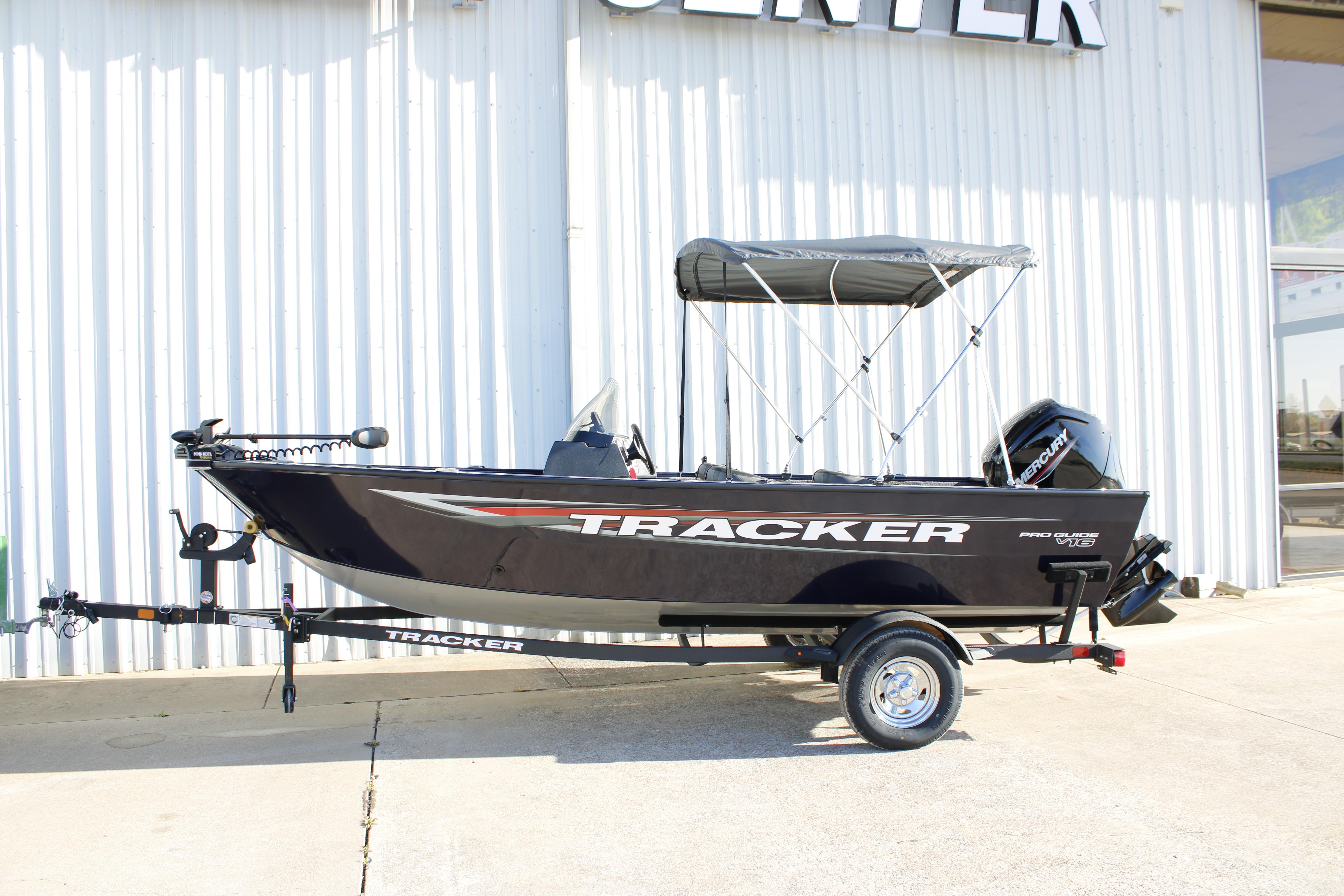 2026 Tracker Pro Guide V-16 SC boat with canopy, parked on trailer outside a building.
