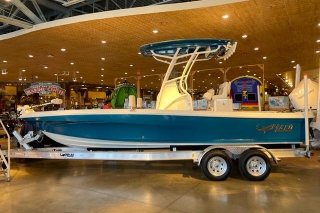 2026 Mako 24 APEX boat on trailer in showroom, blue and white design.