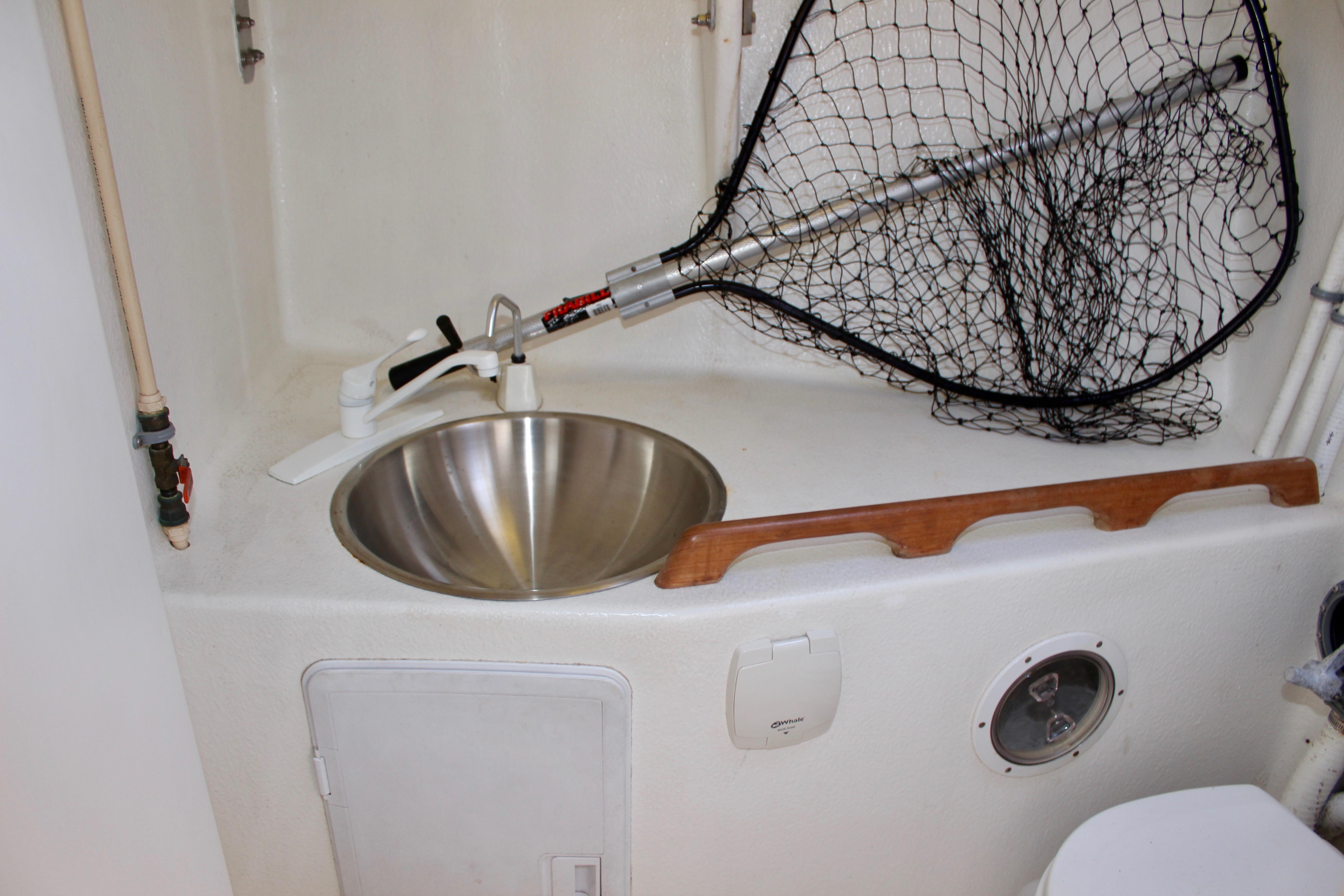 Compact boat bathroom with stainless steel sink, fishing net, and wooden rail on a 1993 Freya 39.