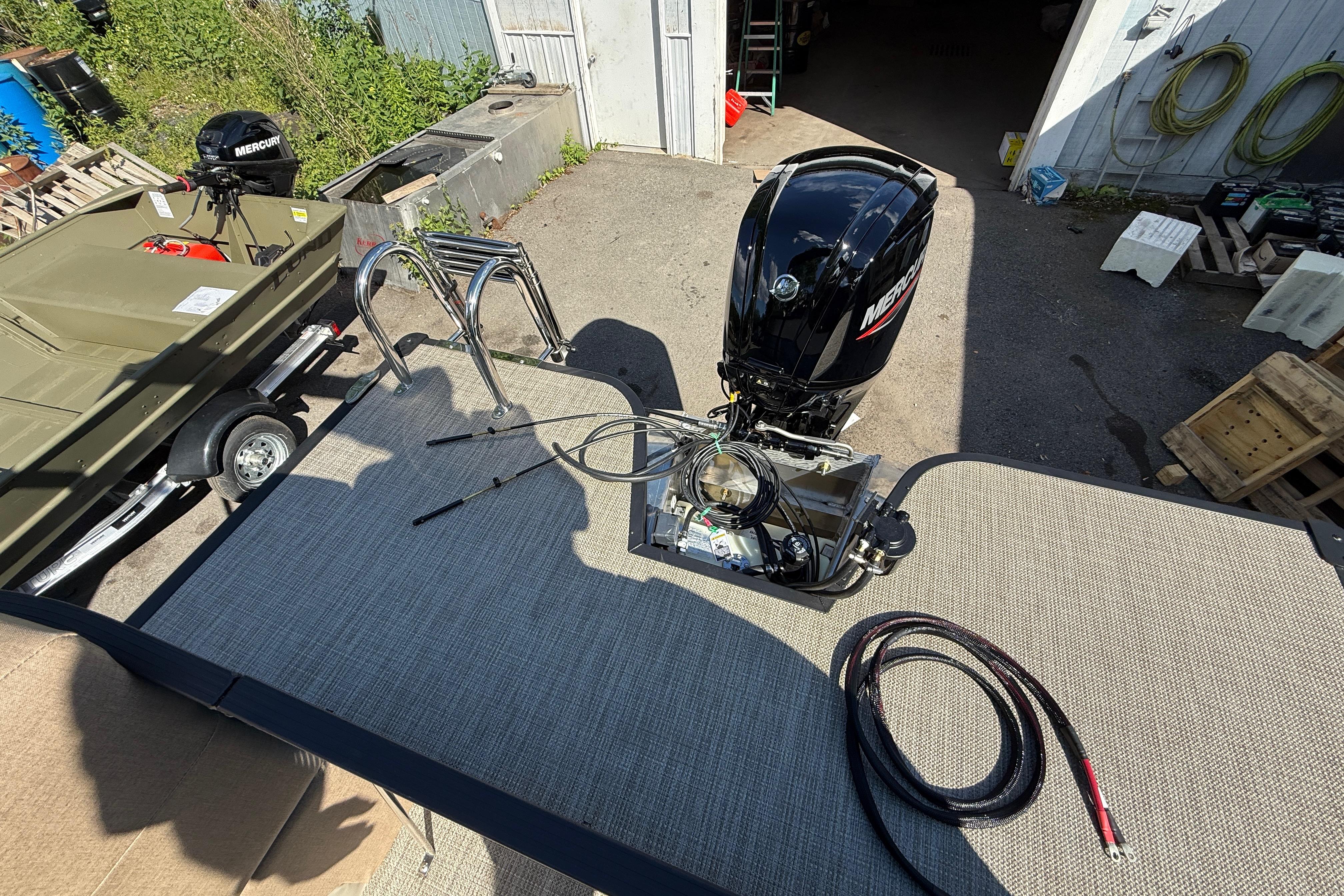 2027 Manitou Aurora RF 23 boat with Mercury outboard motor in a workshop setting.