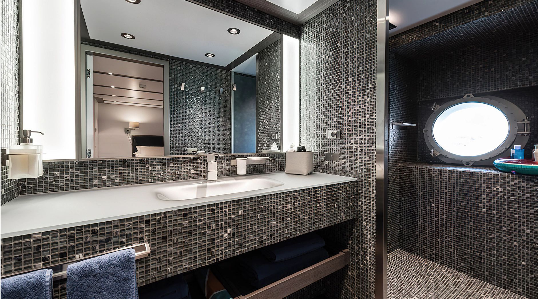 Luxurious bathroom with mosaic tiles, sink, and porthole on a yacht.