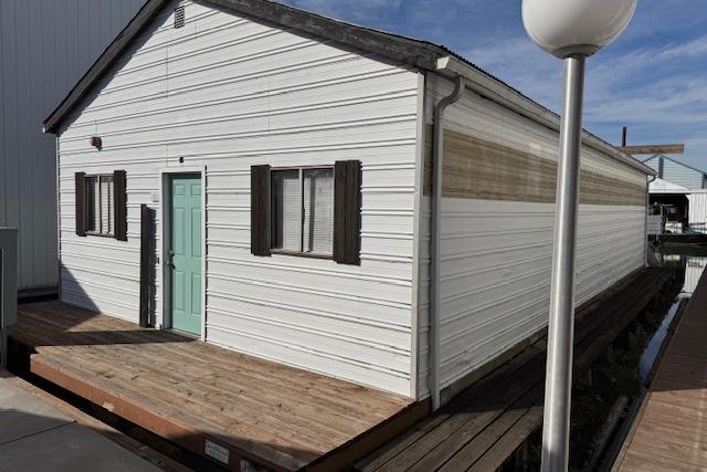 1960 custom boathouse with white siding, teal door, and wooden deck by the water.