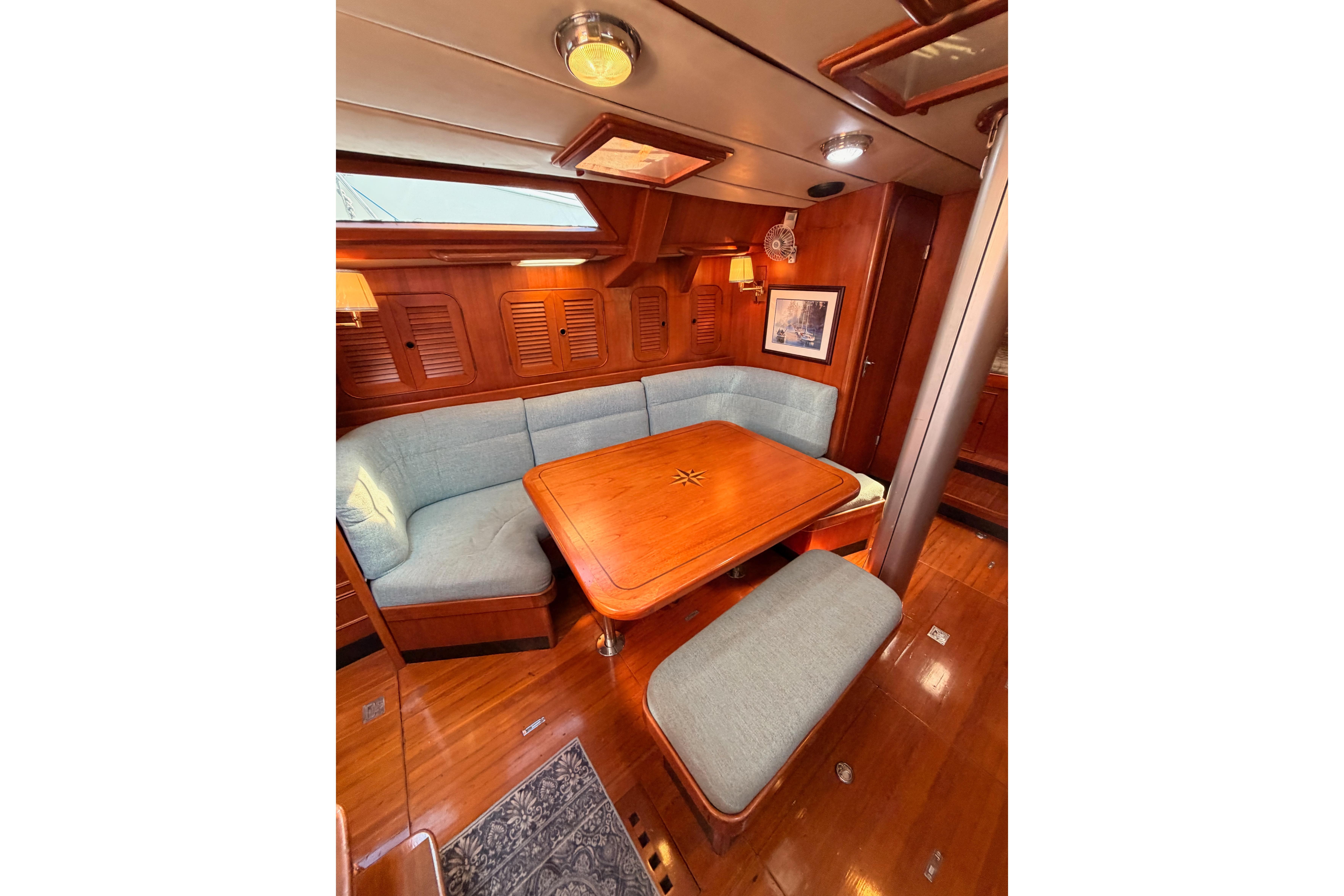 Cozy interior of 1991 Hylas 51 yacht with wooden dining area and cushioned seating.