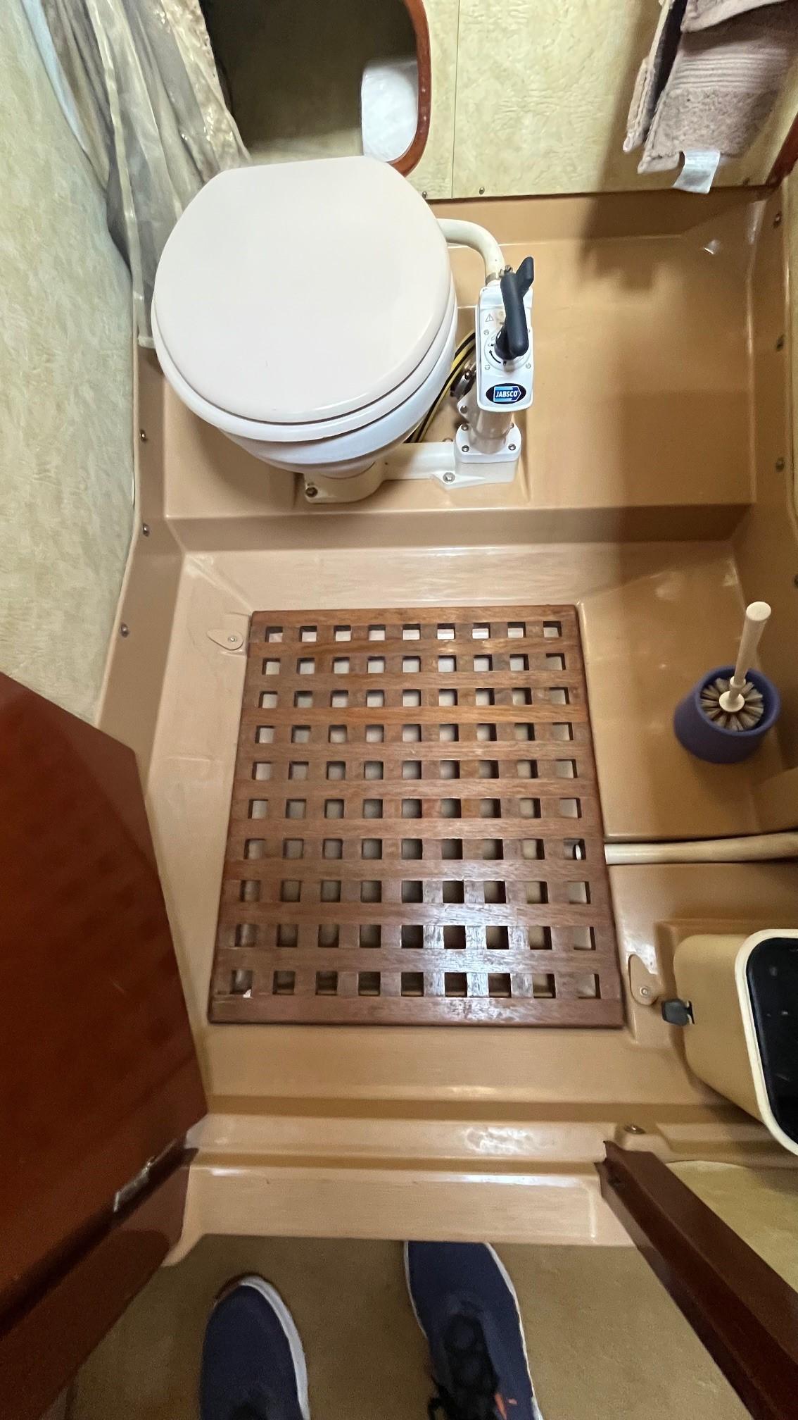 Bathroom interior of a 1996 Amel Super Maramu-53 yacht with toilet and wooden floor grate.