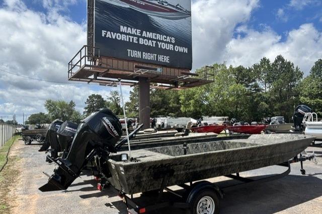 2026 Tracker Grizzly 1860 Utility boat on trailer near billboard under cloudy sky.