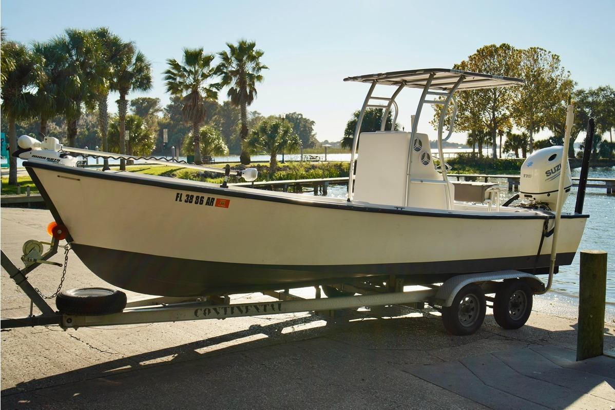 1970 Aquasport 222 Flatback boat on trailer by waterfront with palm trees.
