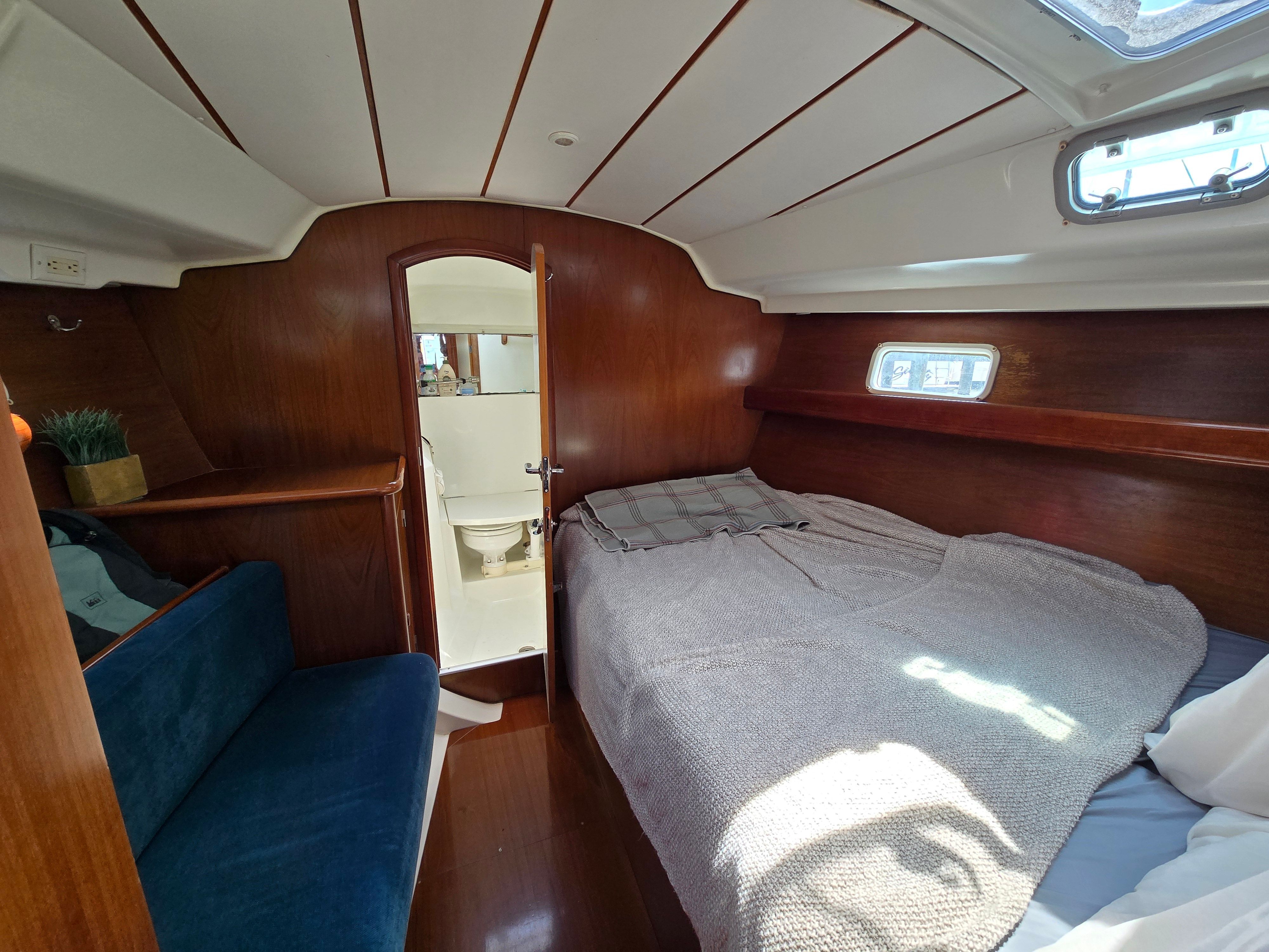 Interior of a 1998 Beneteau 411 with a cozy bed and wooden walls.