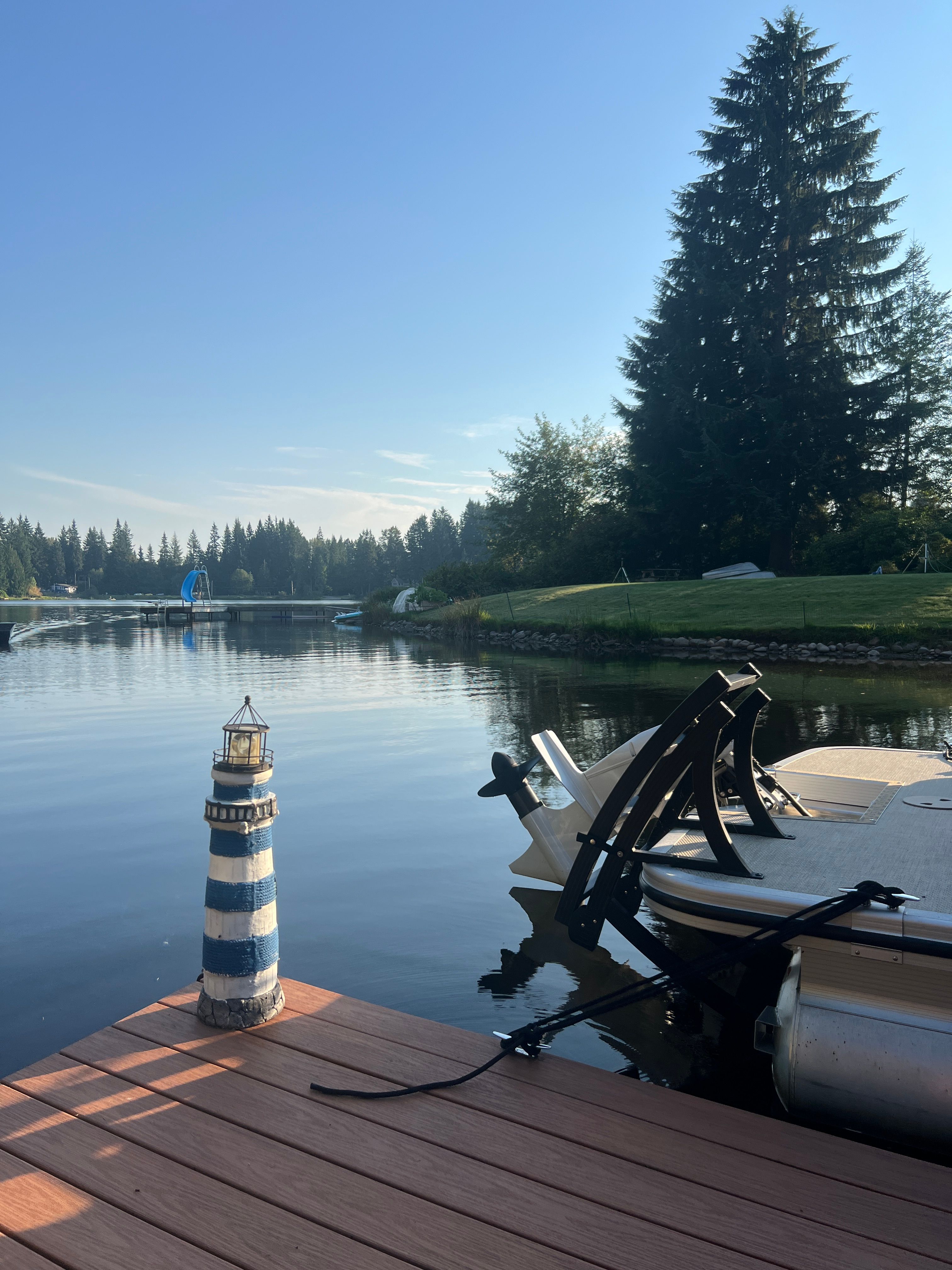 A boat is docked at a serene lakeside with a lighthouse ornament on the dock.