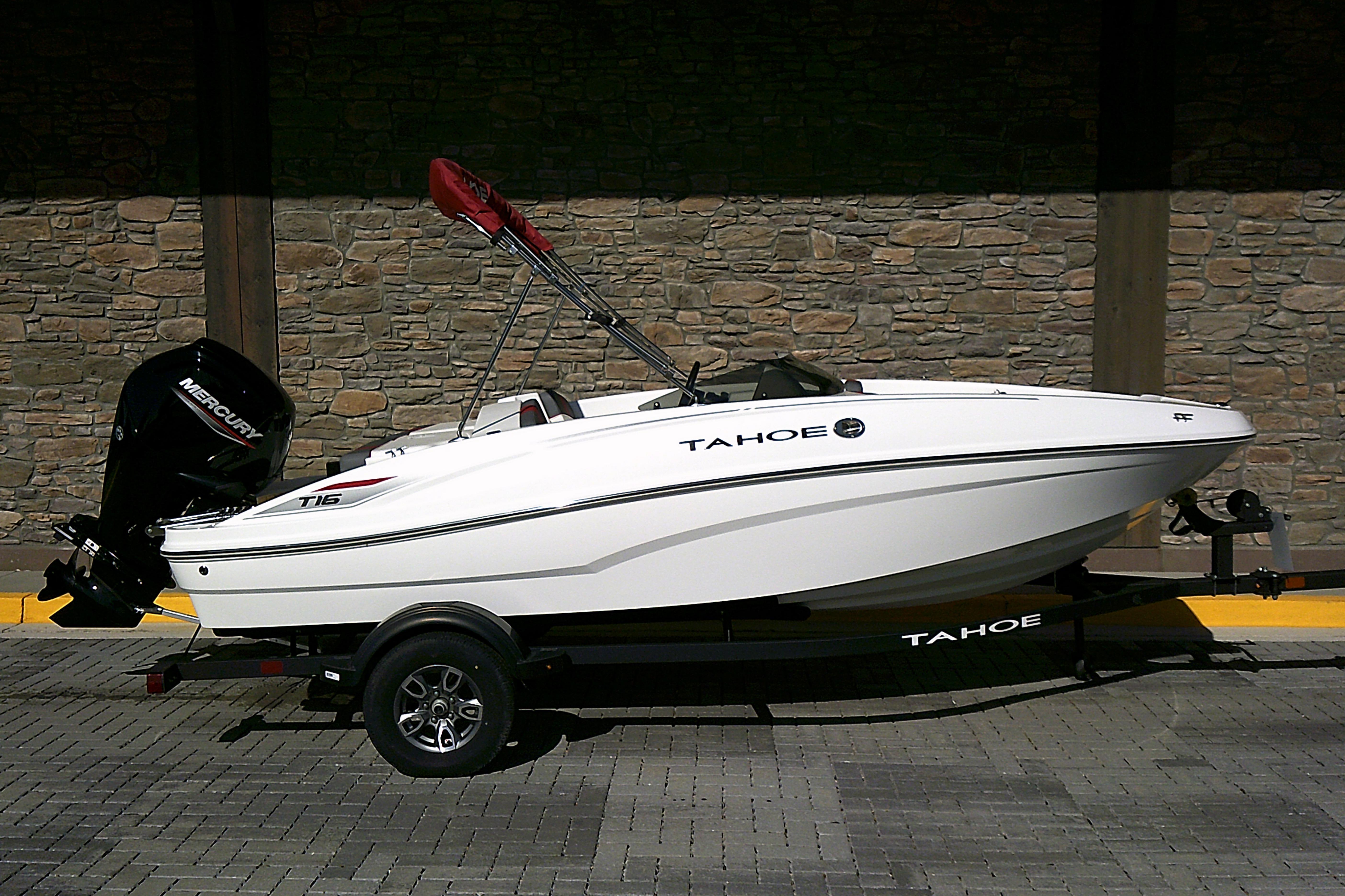 2025 Tahoe T16 boat on trailer, parked against stone wall background.