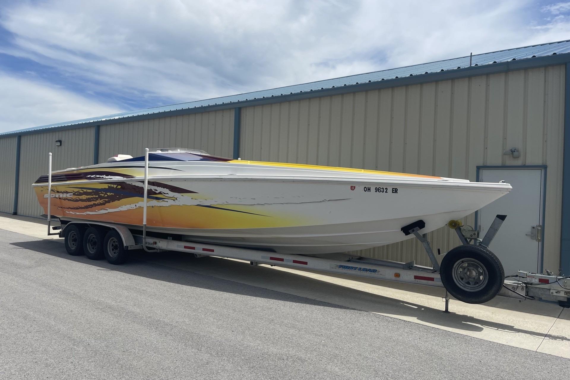 2006 Sonic 386 boat on trailer, vibrant yellow and orange design, parked near a building.