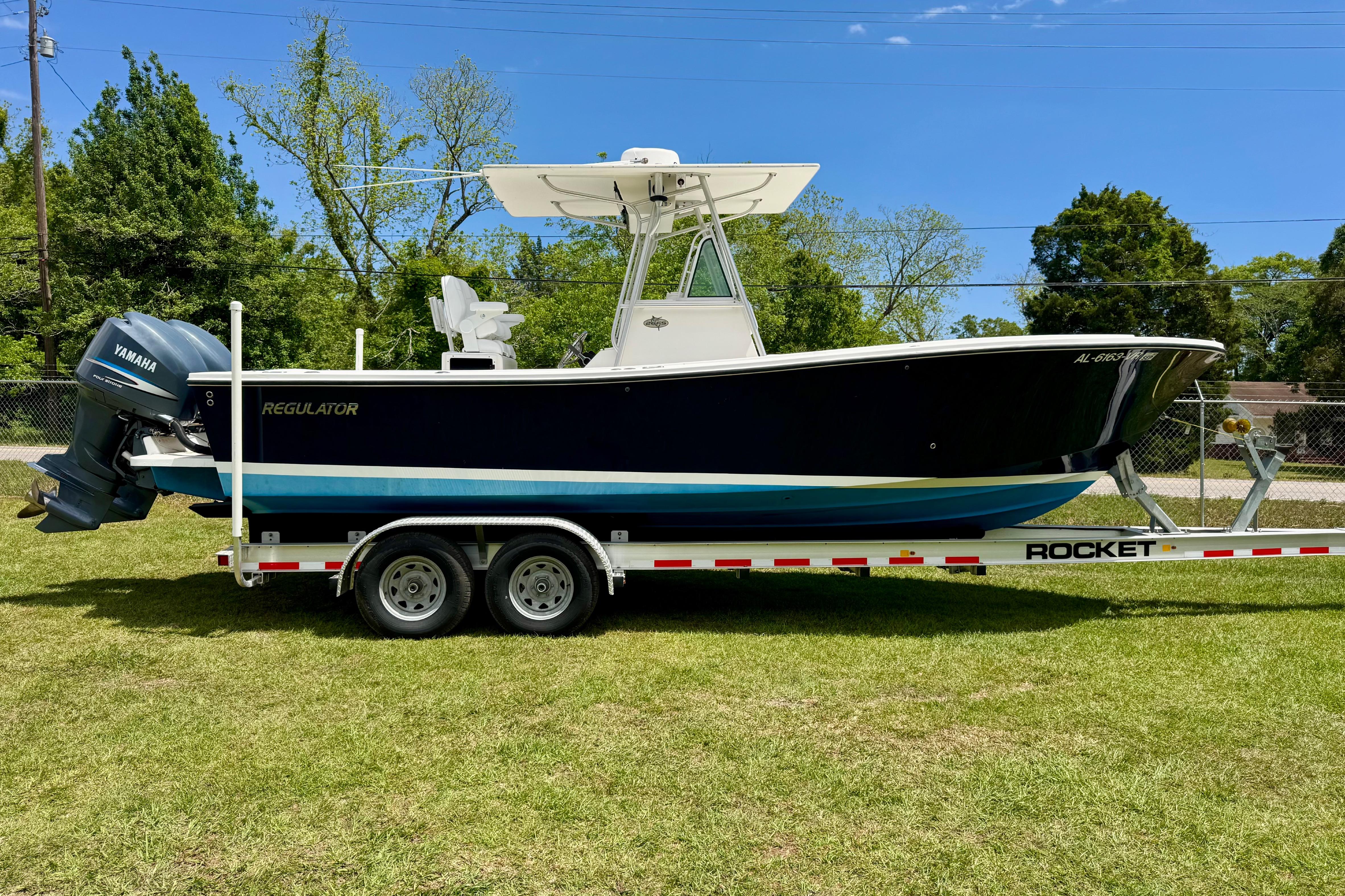 2000 Regulator 26 Forward Seating boat on trailer, parked on grass with trees in background.