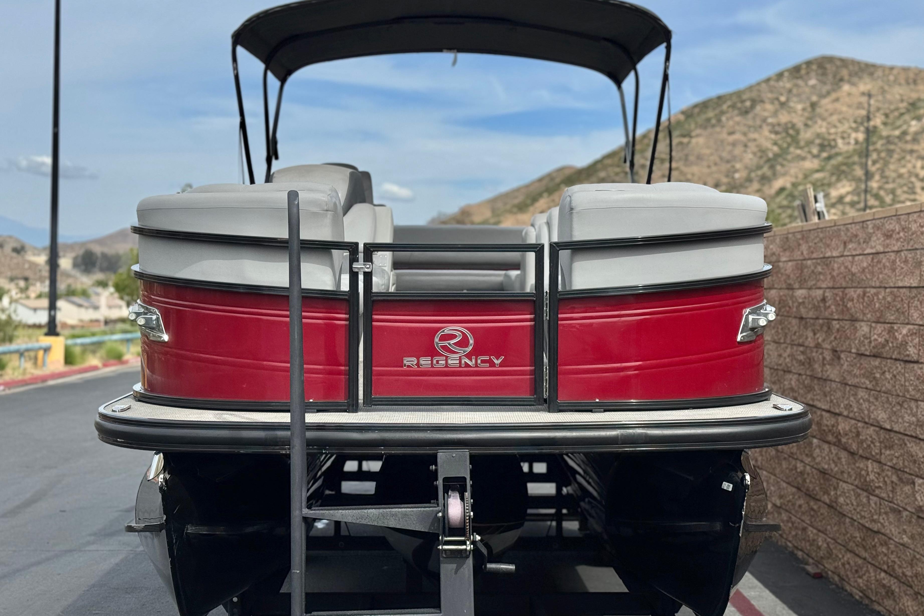 2022 Regency 250 DL3 pontoon boat, red exterior, parked with scenic mountain backdrop.