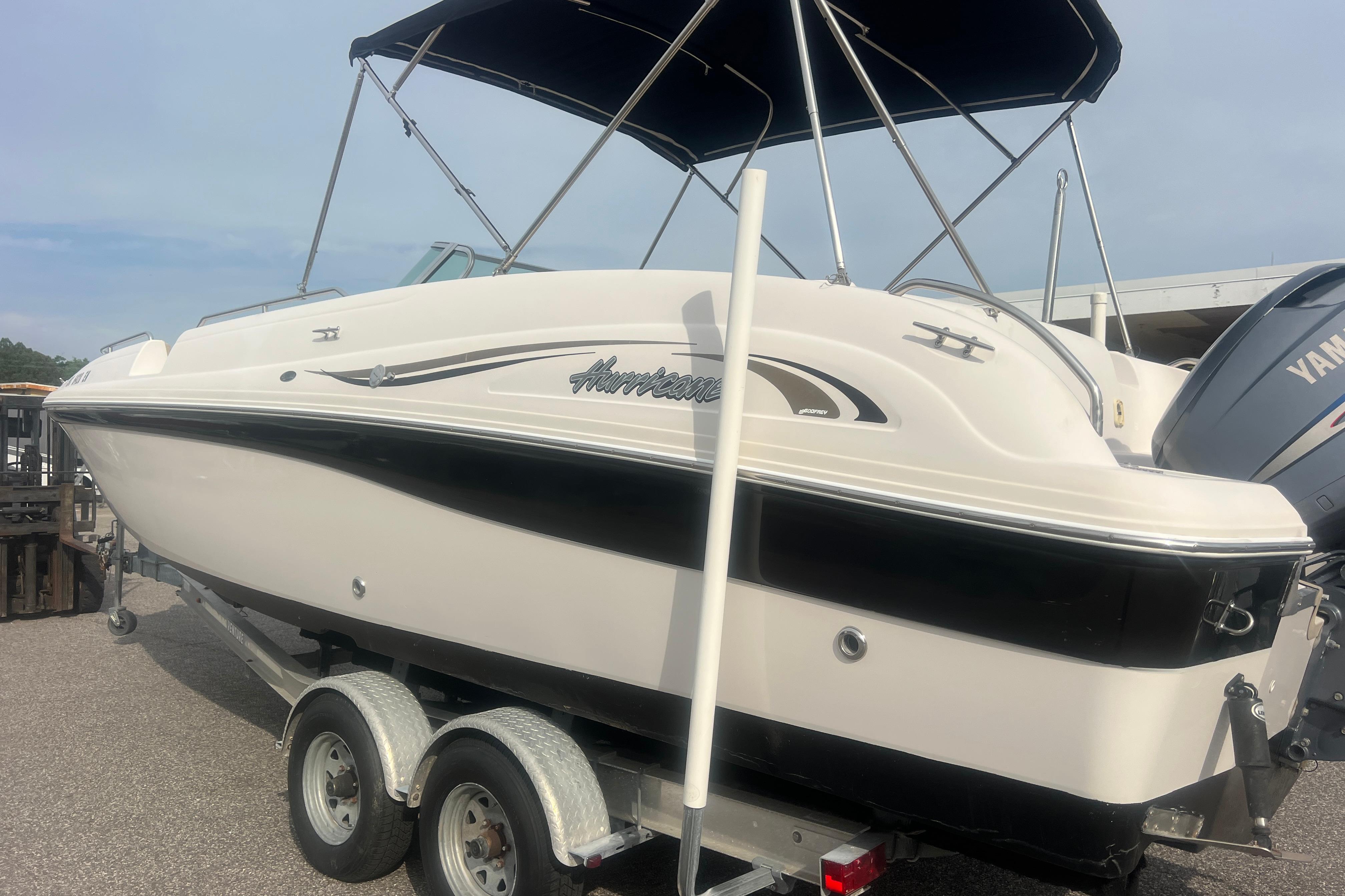 2002 Hurricane SunDeck 260 OB boat on trailer with canopy, parked outdoors.