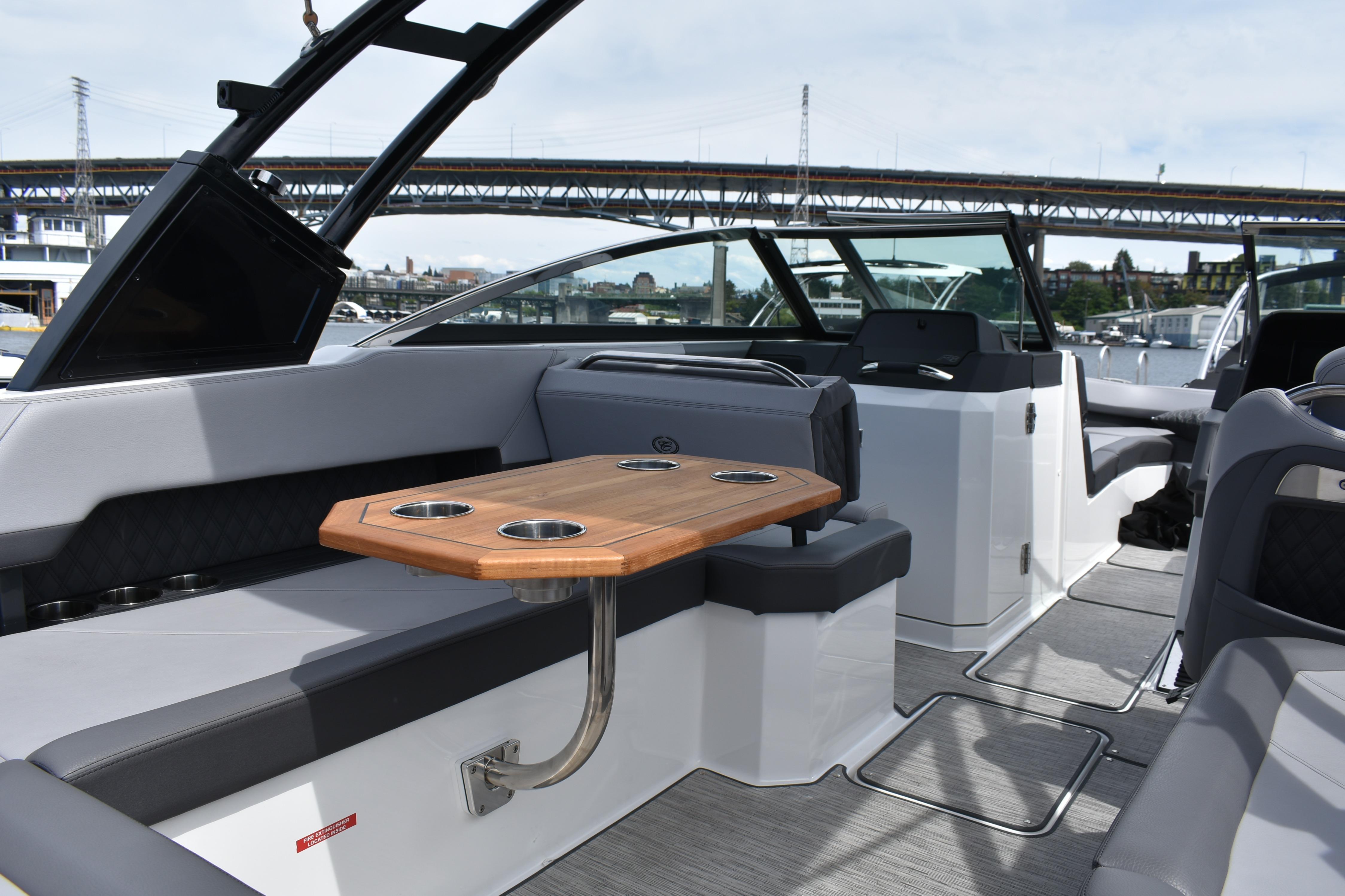 Interior of 2023 Cobalt R8 boat with seating and wooden table, under a bridge.