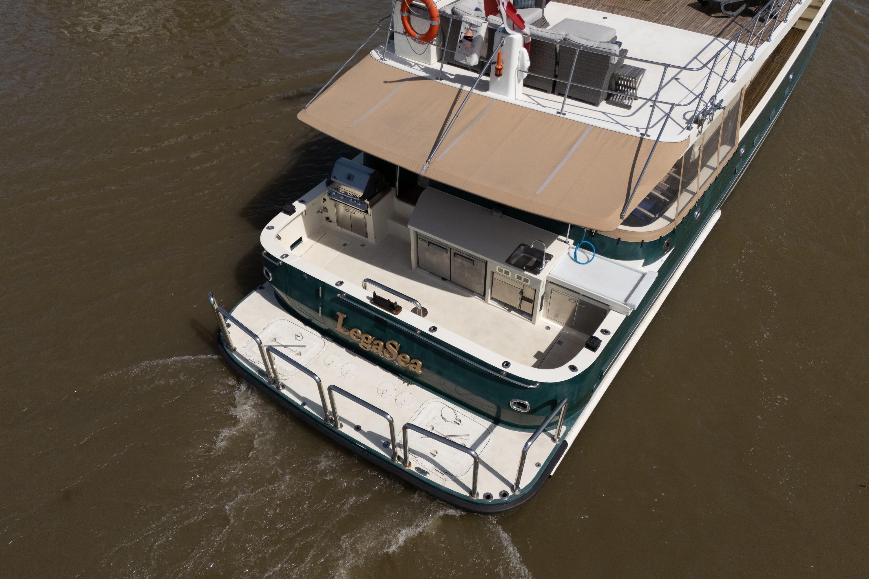 1985 Delta Marine Expedition Yacht cruising on brown water, featuring outdoor deck and canopy.