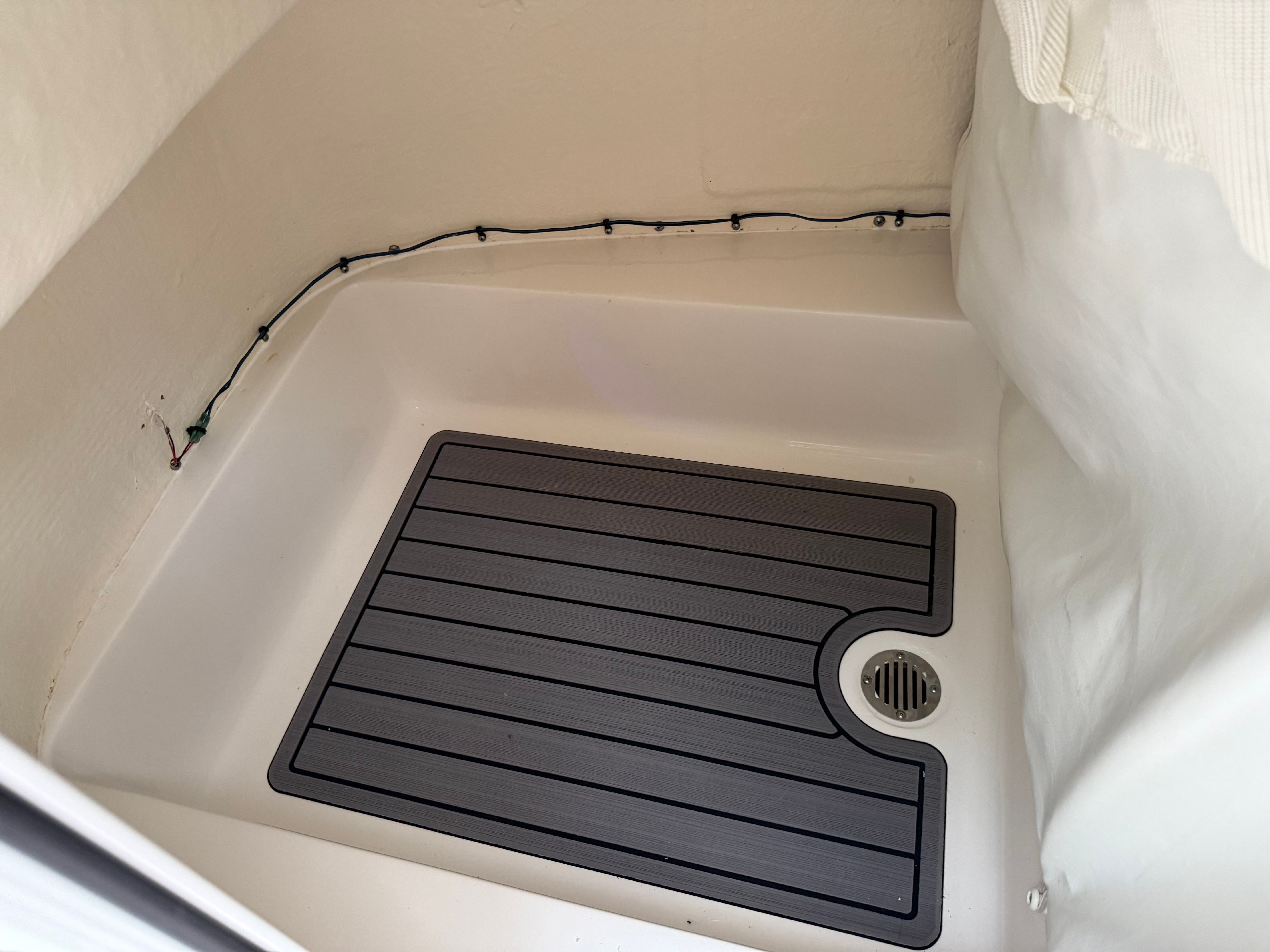 Shower area with a gray non-slip mat and drain in a boat cabin.