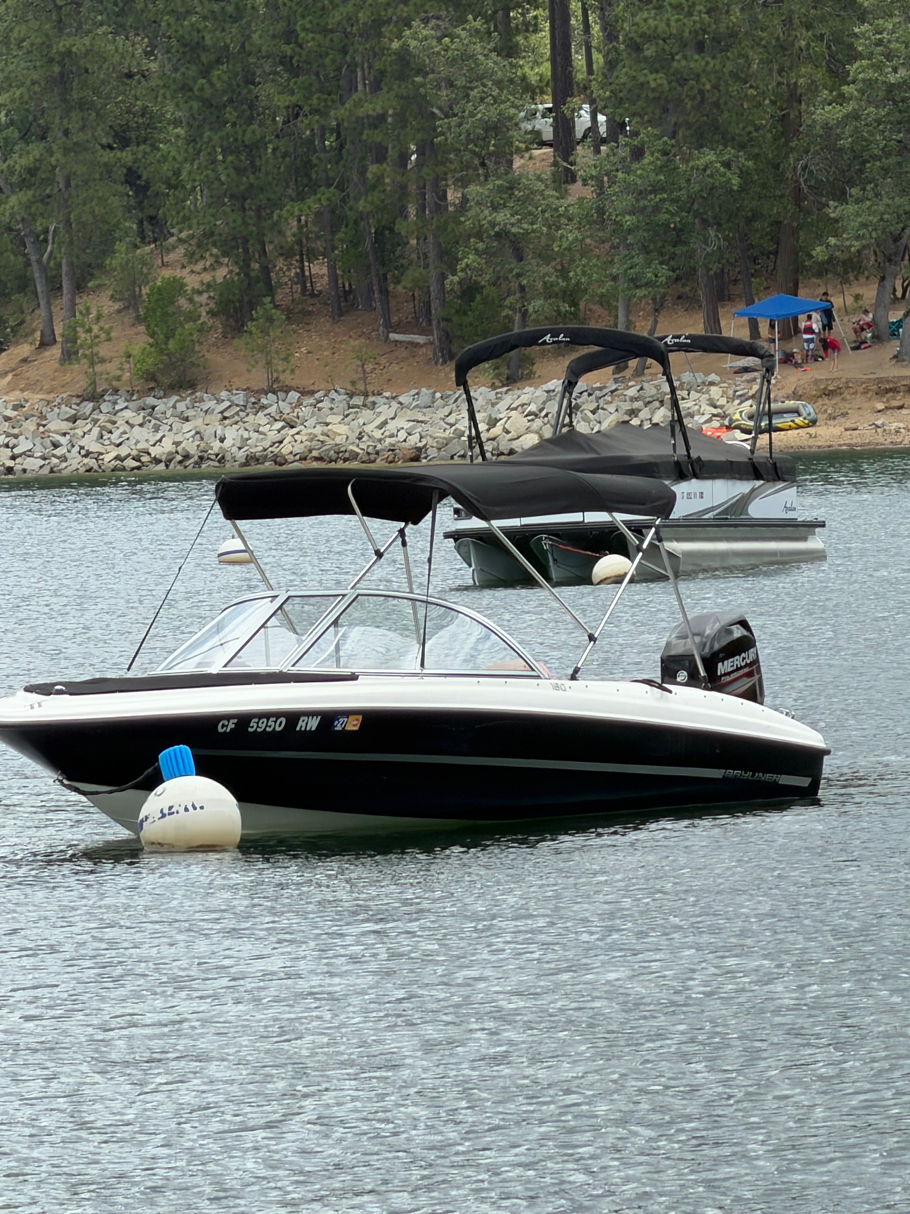 A 2016 Bayliner 160 Bowrider floats on a calm lake, surrounded by trees.