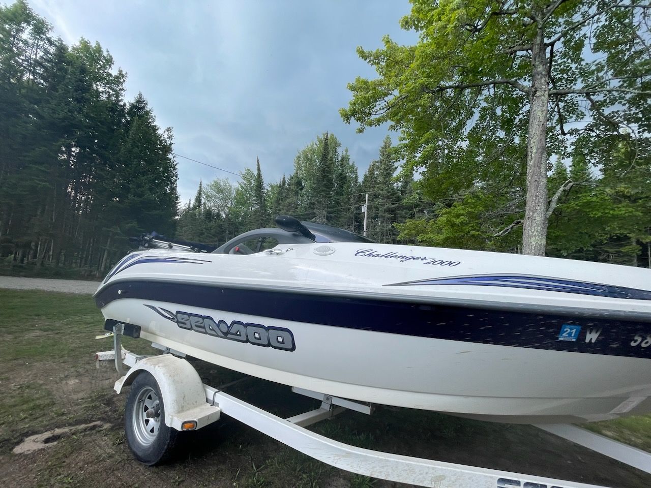 2004 Bombardier Challenger boat on trailer, surrounded by lush green trees.