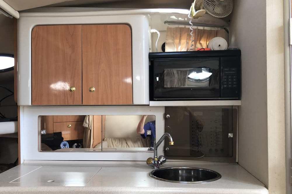1999 Regal Commodore 2760 boat kitchen with cabinets, microwave, sink, and countertop.