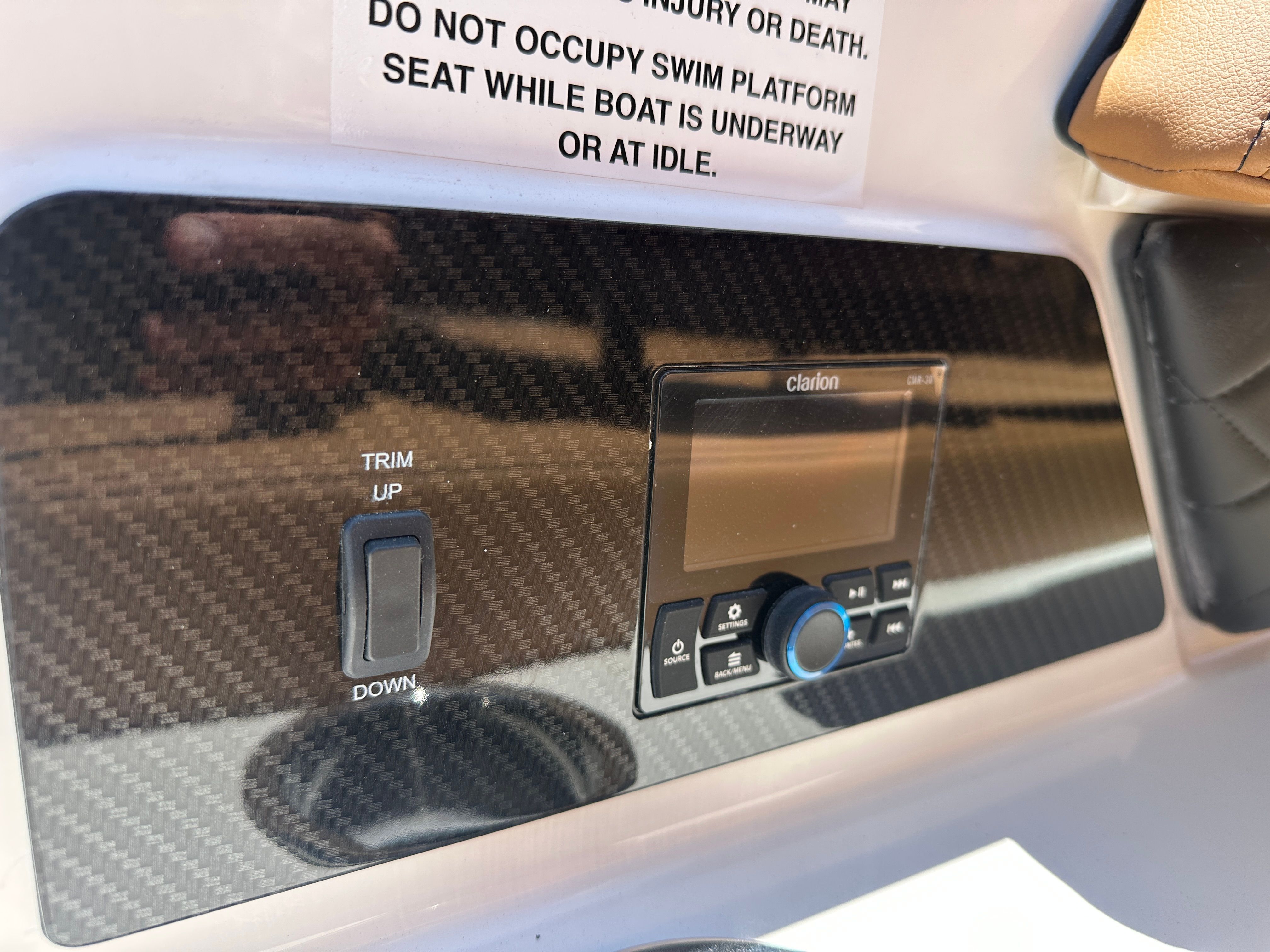 Close-up of a boat control panel with a Clarion audio system and trim switch.