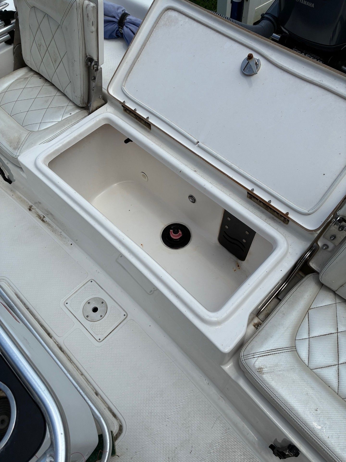 An open storage compartment on a boat with cushioned seats and a round drain.