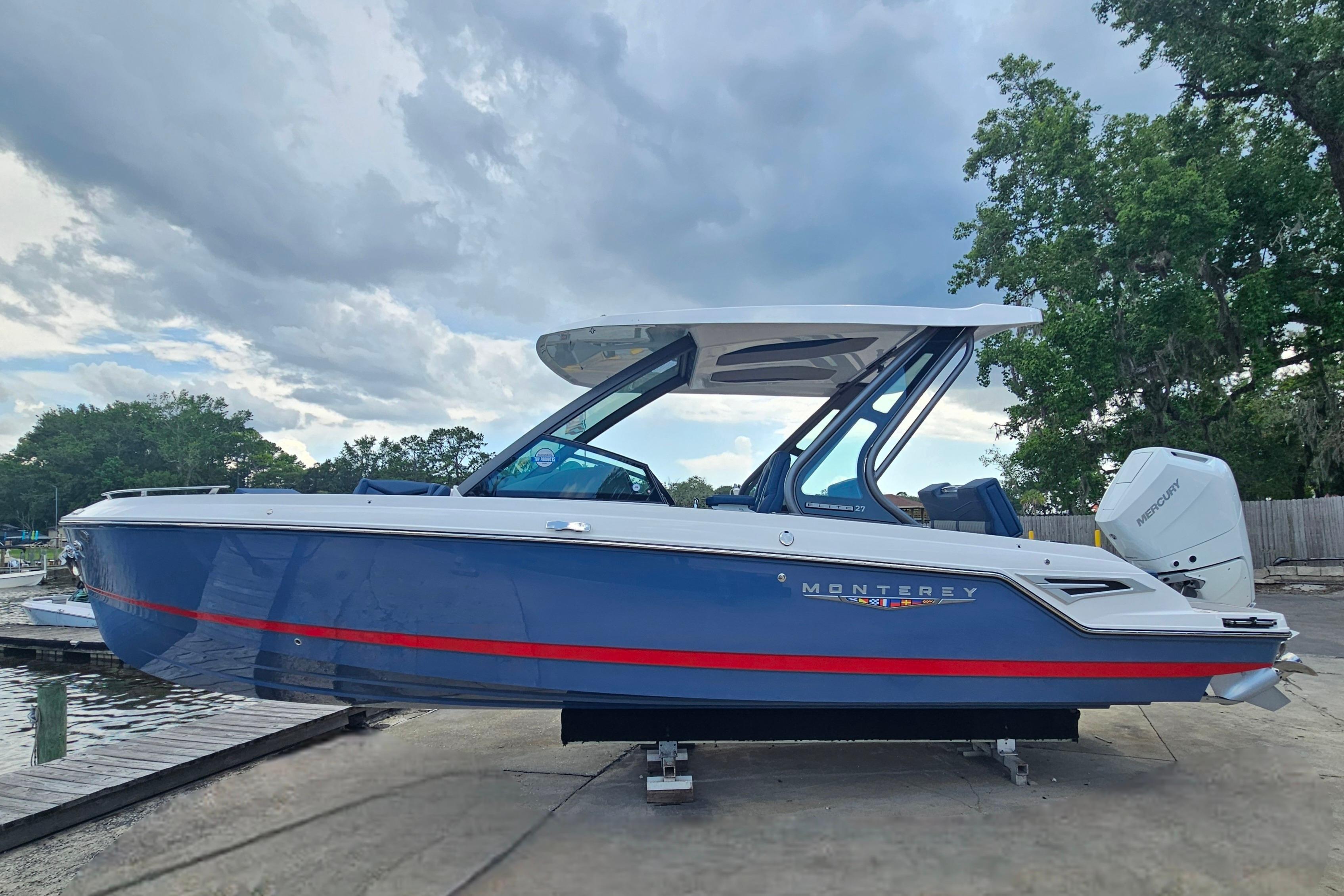 2026 Monterey Elite 27 OB boat with sleek blue design and red stripe, docked outdoors.